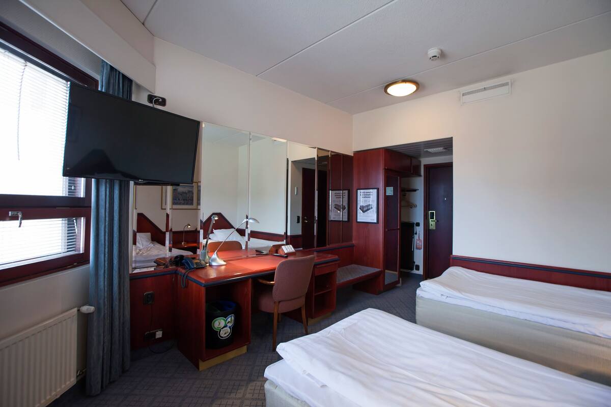A hotel room with a bed, a desk with a chair, a television, and a mirror.