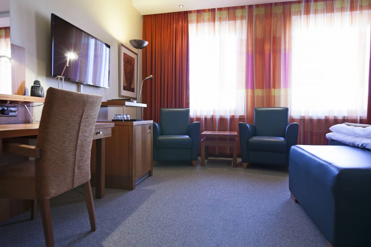 A hotel room with a desk, two chairs, a bed, and a TV.