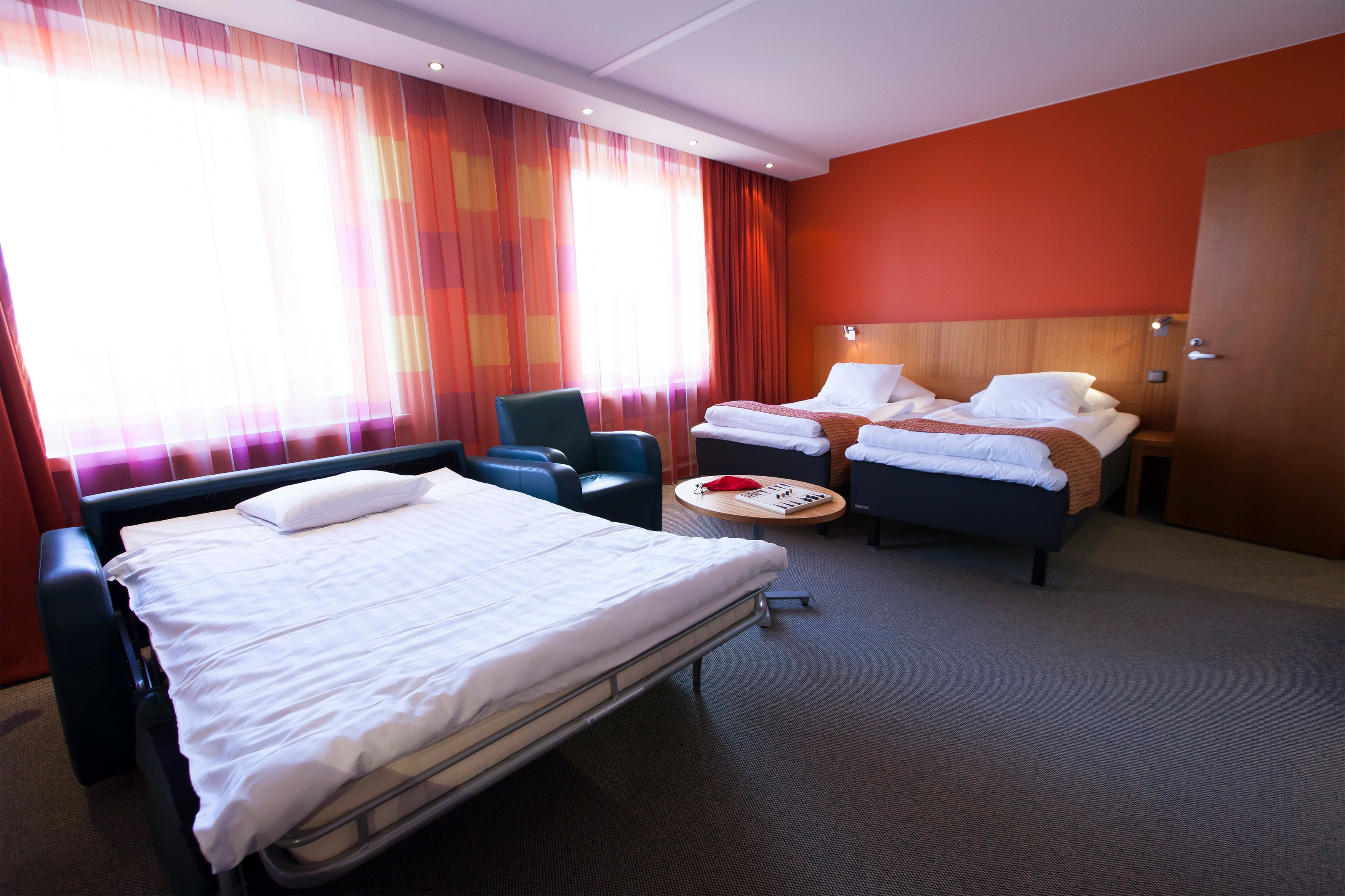 A hotel room with a large bed, two smaller beds, a desk, and a chair.