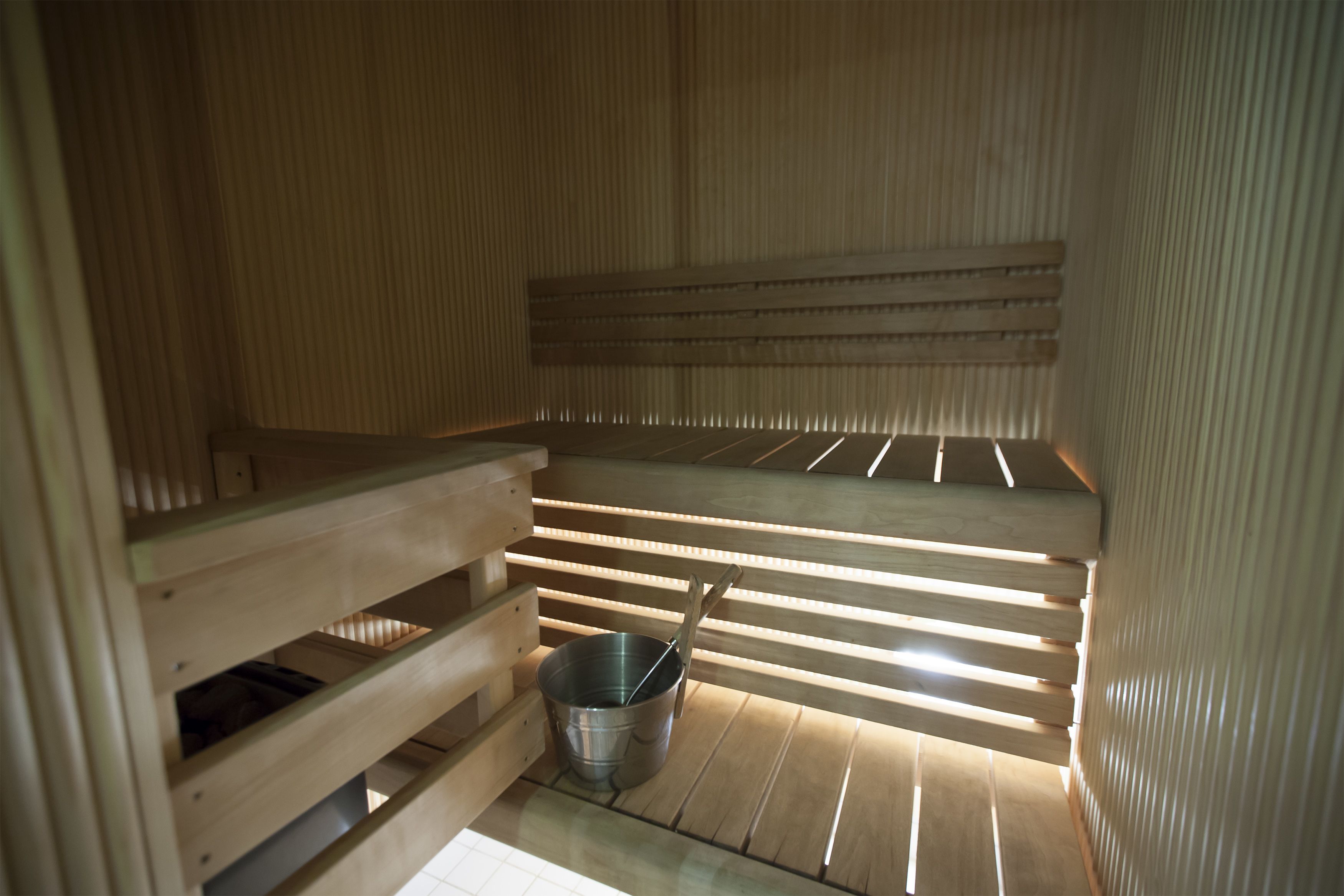 A sauna with wooden benches and a metal bucket.