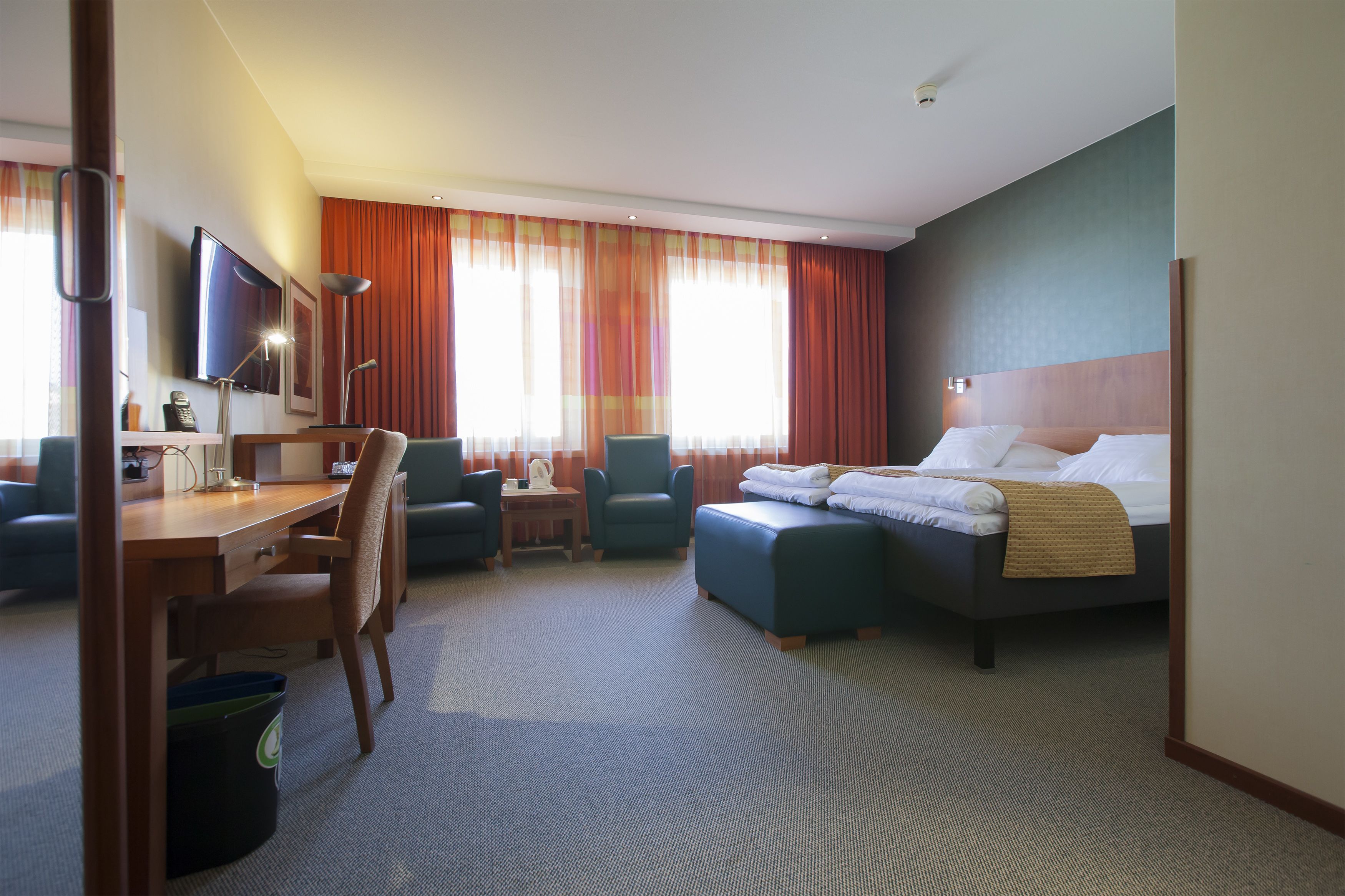 Hotelkamer met een bed, een bureau, twee stoelen, een televisie en een groot raam met gordijnen.