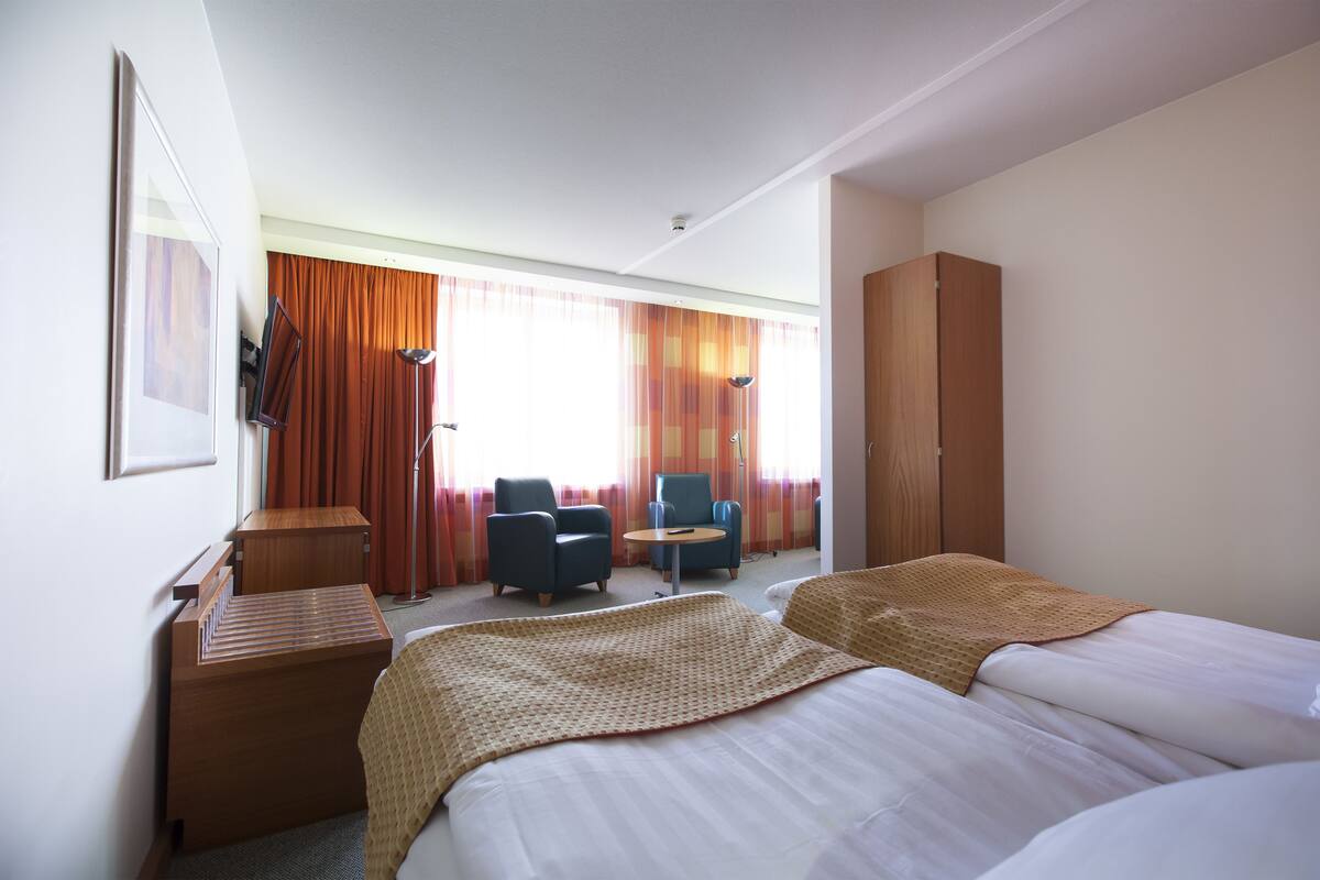 A hotel room with two beds, a desk, a chair, and a wardrobe.