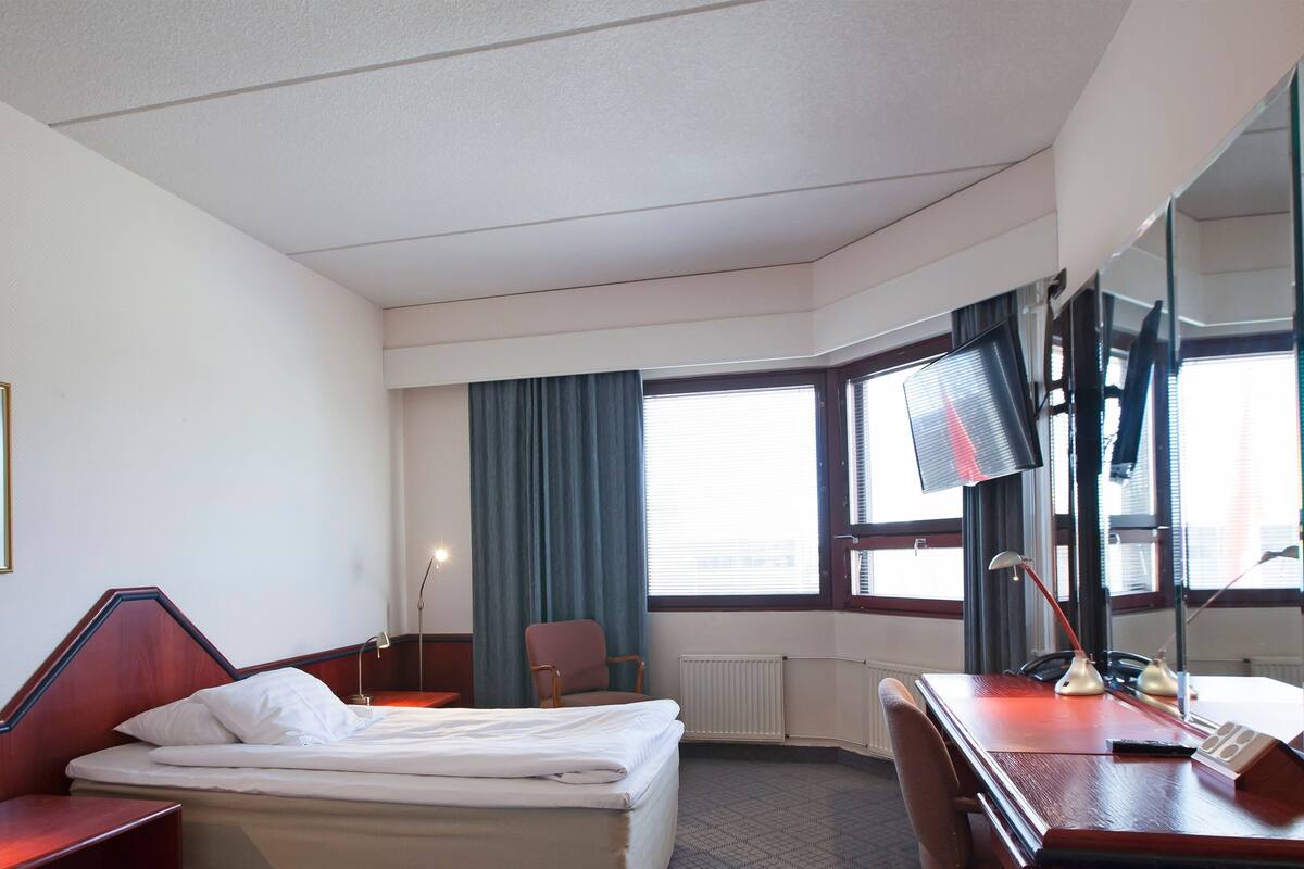 A hotel room with a bed, desk, chair, and a large mirror.