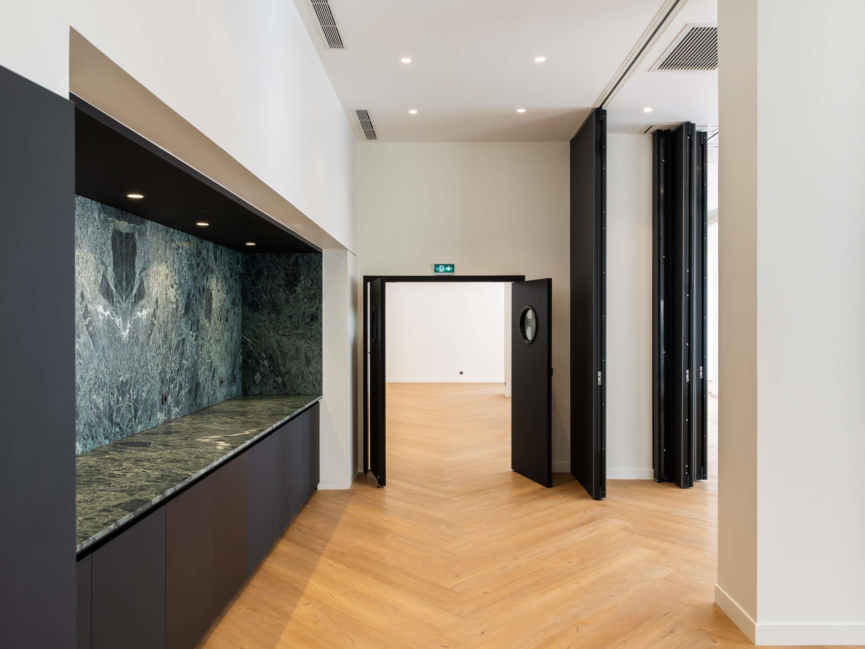 Un couloir avec un mur en marbre, un plancher en bois et une porte donnant sur une autre pièce.