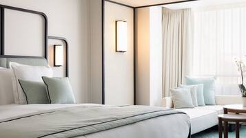 A modern hotel room with a large bed, a sofa, a small table, and a window with curtains.