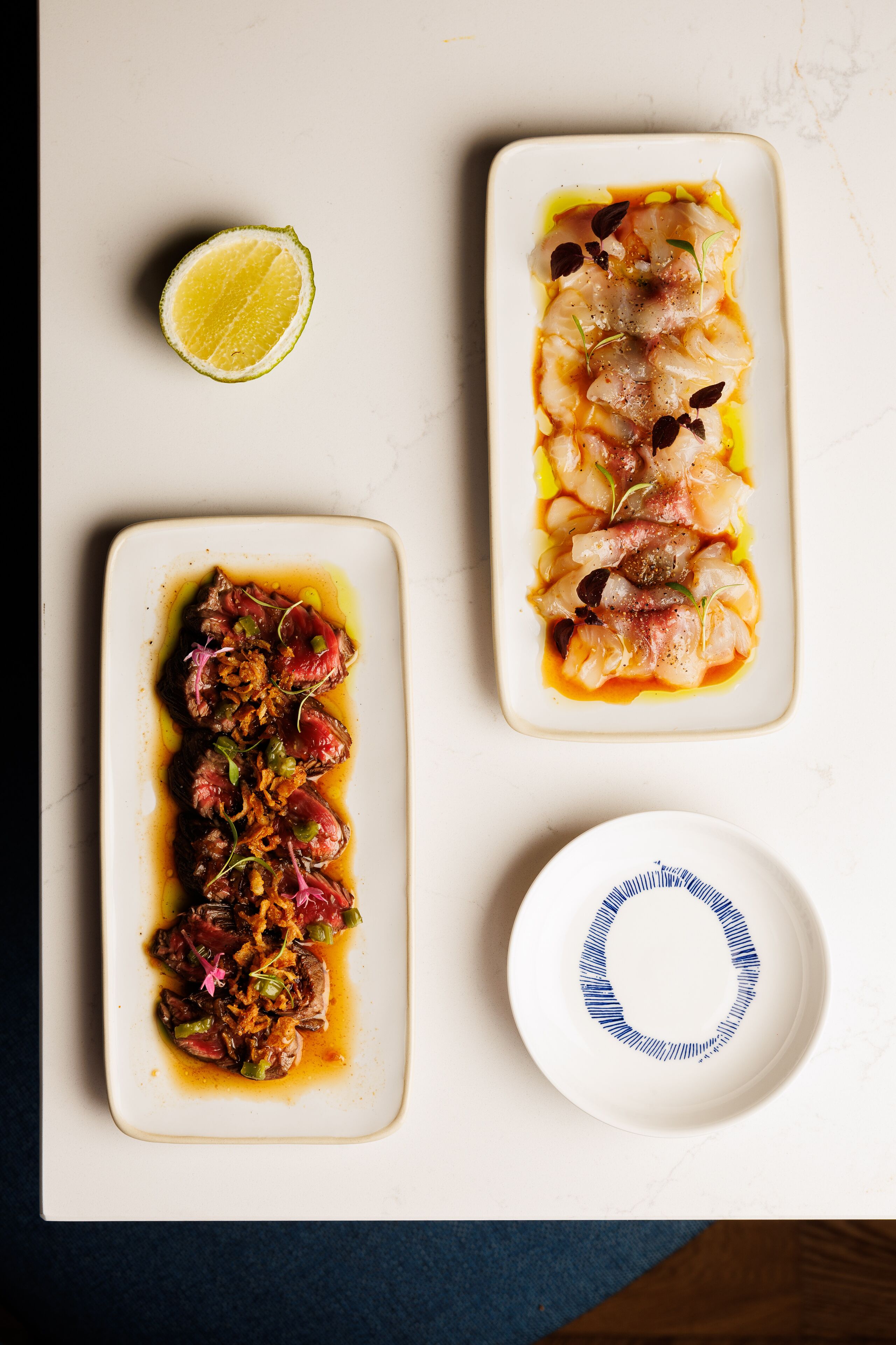 A table with three rectangular dishes of food, a small bowl with a blue pattern, and a half-cut lime.
