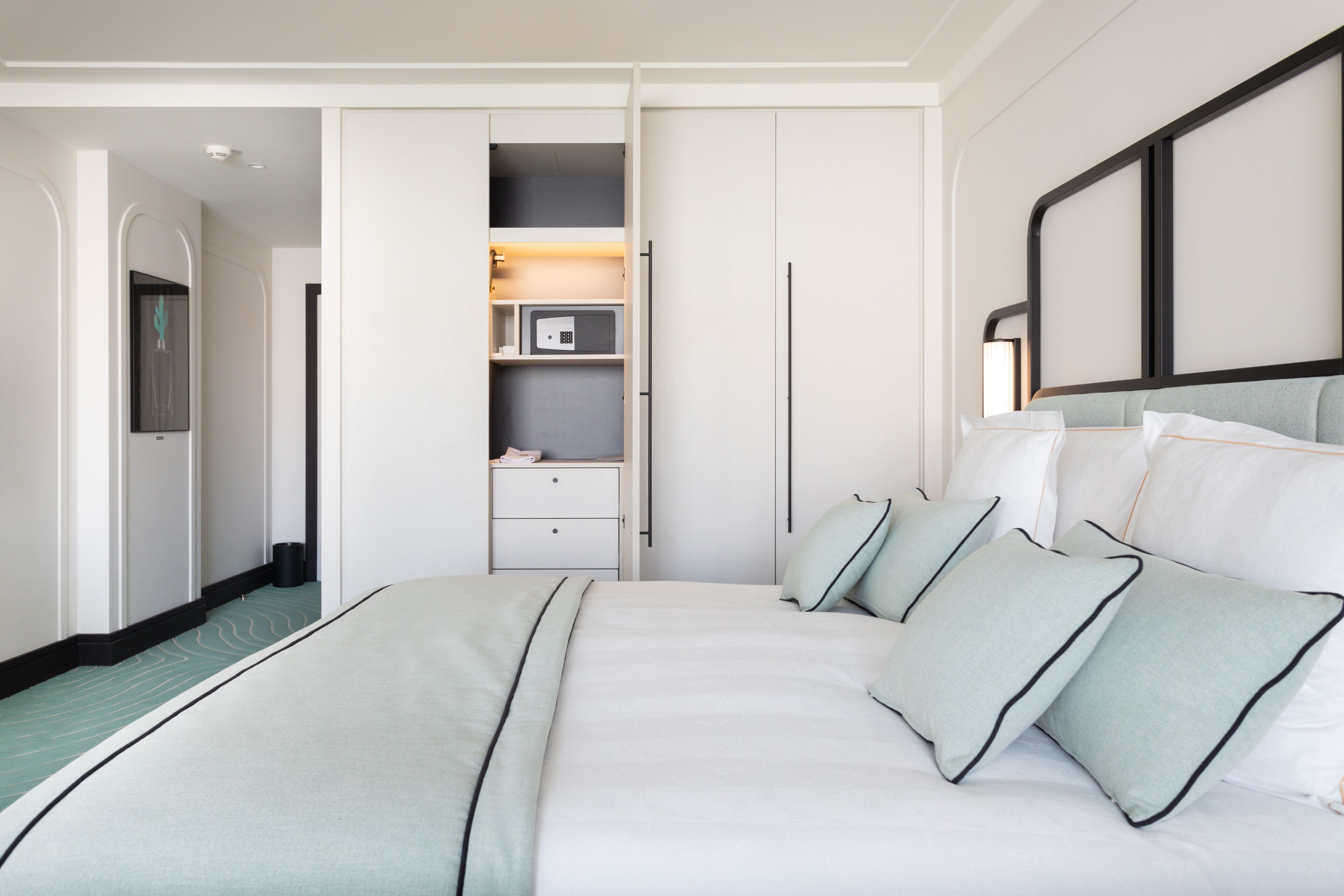 A modern hotel room with a large bed, a wardrobe, a vanity, and a mirror.