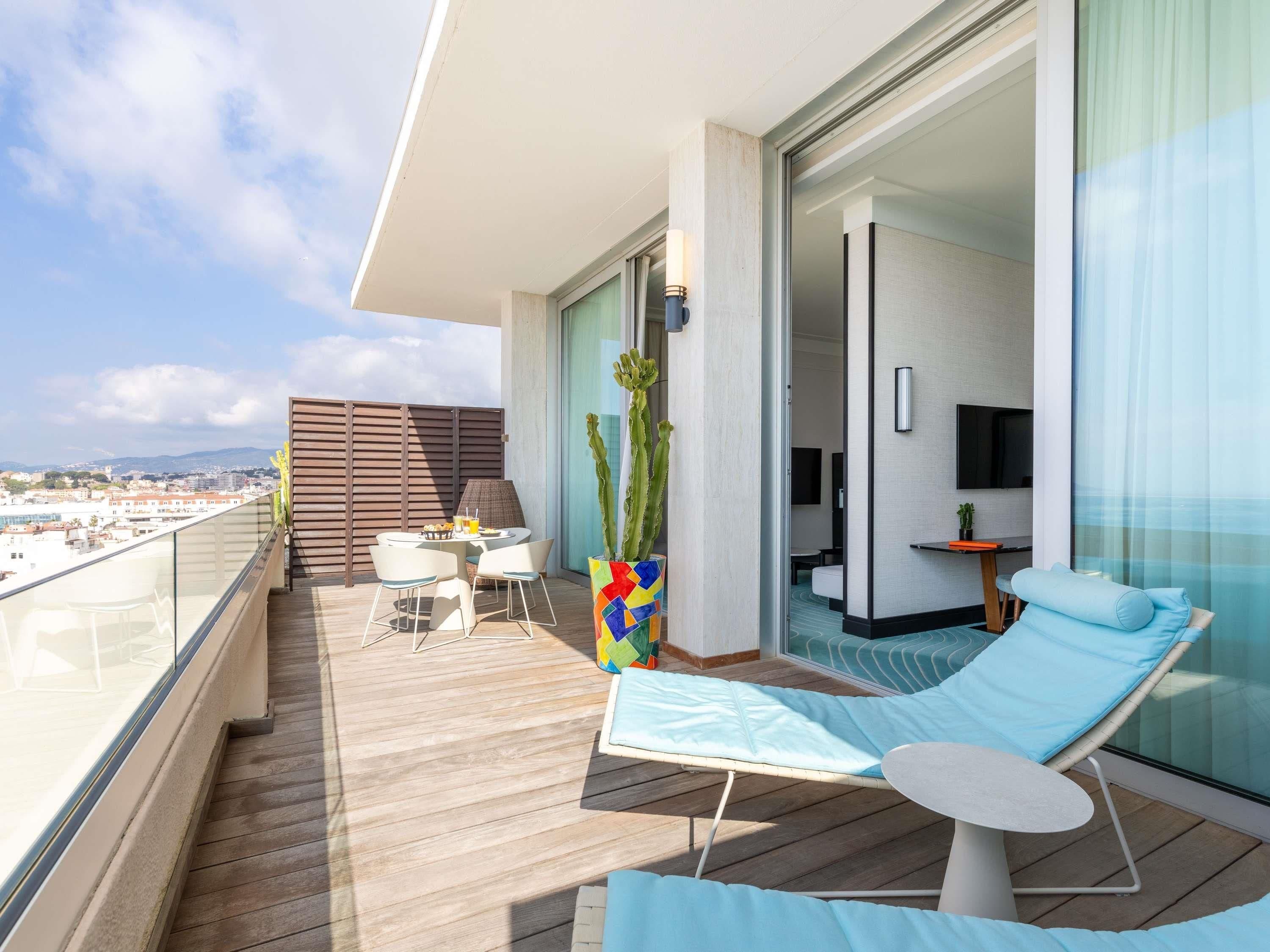 A balcony with a wooden floor, a table with chairs, a sofa, a TV, and a plant.