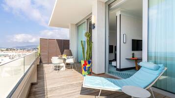 A balcony with a wooden floor, a table with chairs, a sofa, a TV, and a plant.