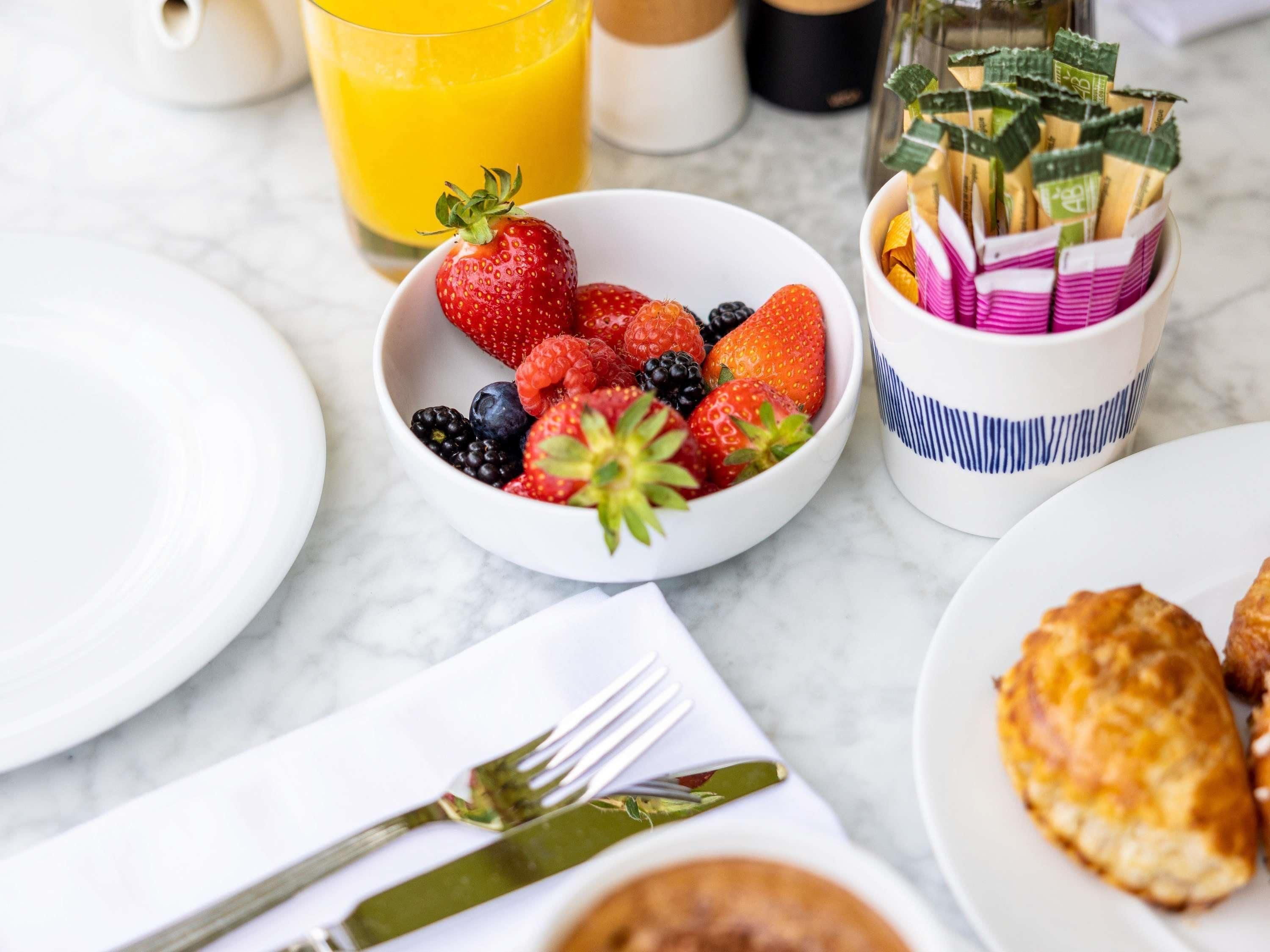 A breakfast setting with a bowl of mixed berries, a glass of orange juice, and a cup with tea bags.
