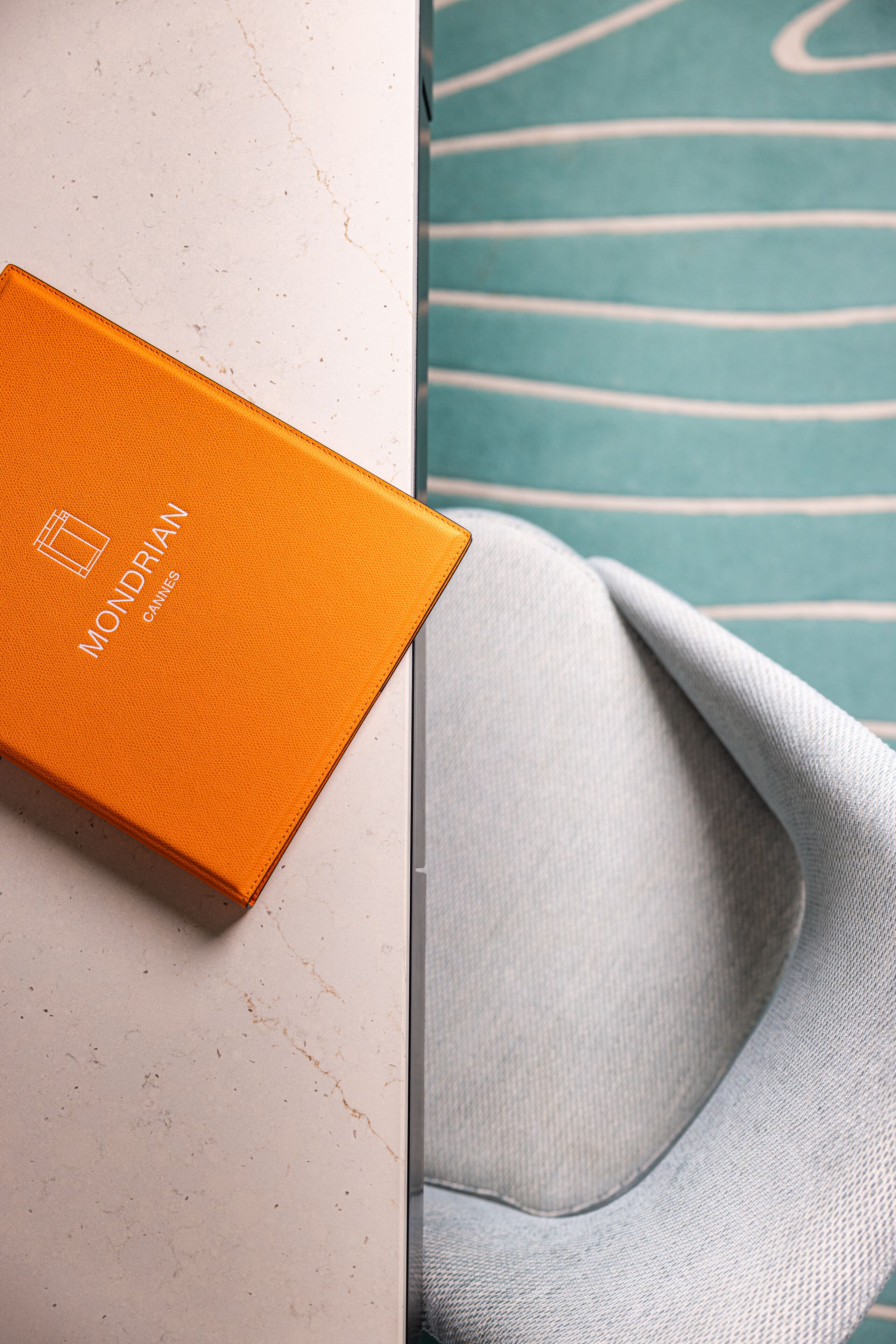 A white marble surface with a folded grey fabric and an orange box with "Mondrian" text.