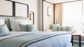 Een moderne hotelkamer met een groot bed, een klein tafeltje en uitzicht op de stad door grote ramen.