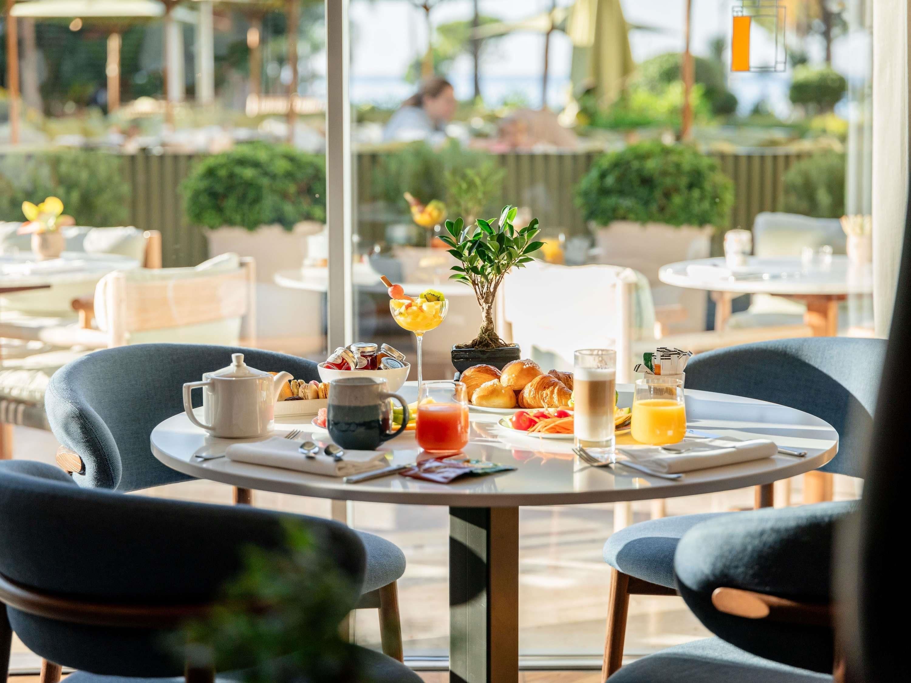 A dining table with breakfast items, a potted plant, and a view of the outdoors.
