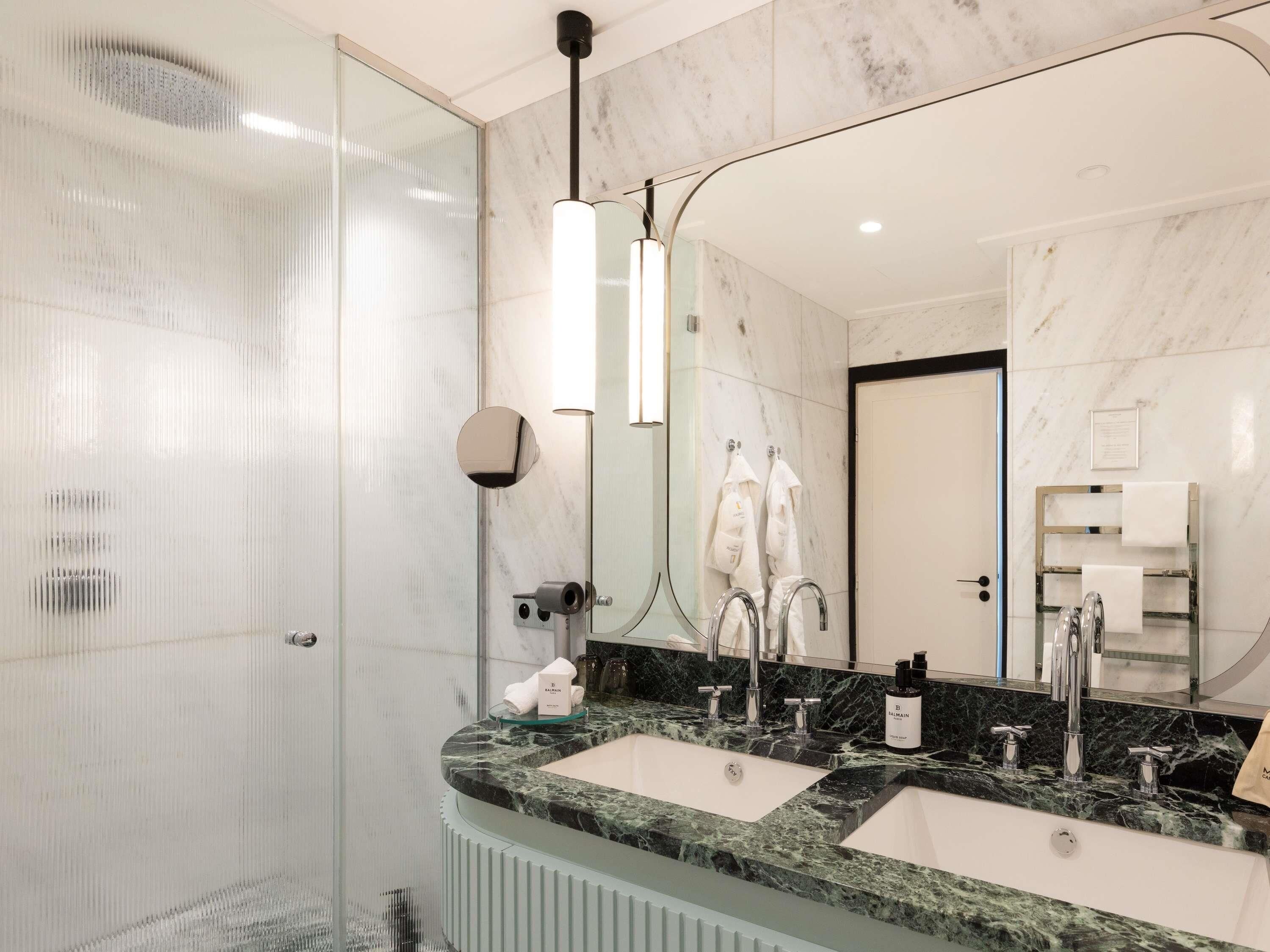 A modern bathroom with a glass shower enclosure, two sinks with marble countertops, and a large mirror.
