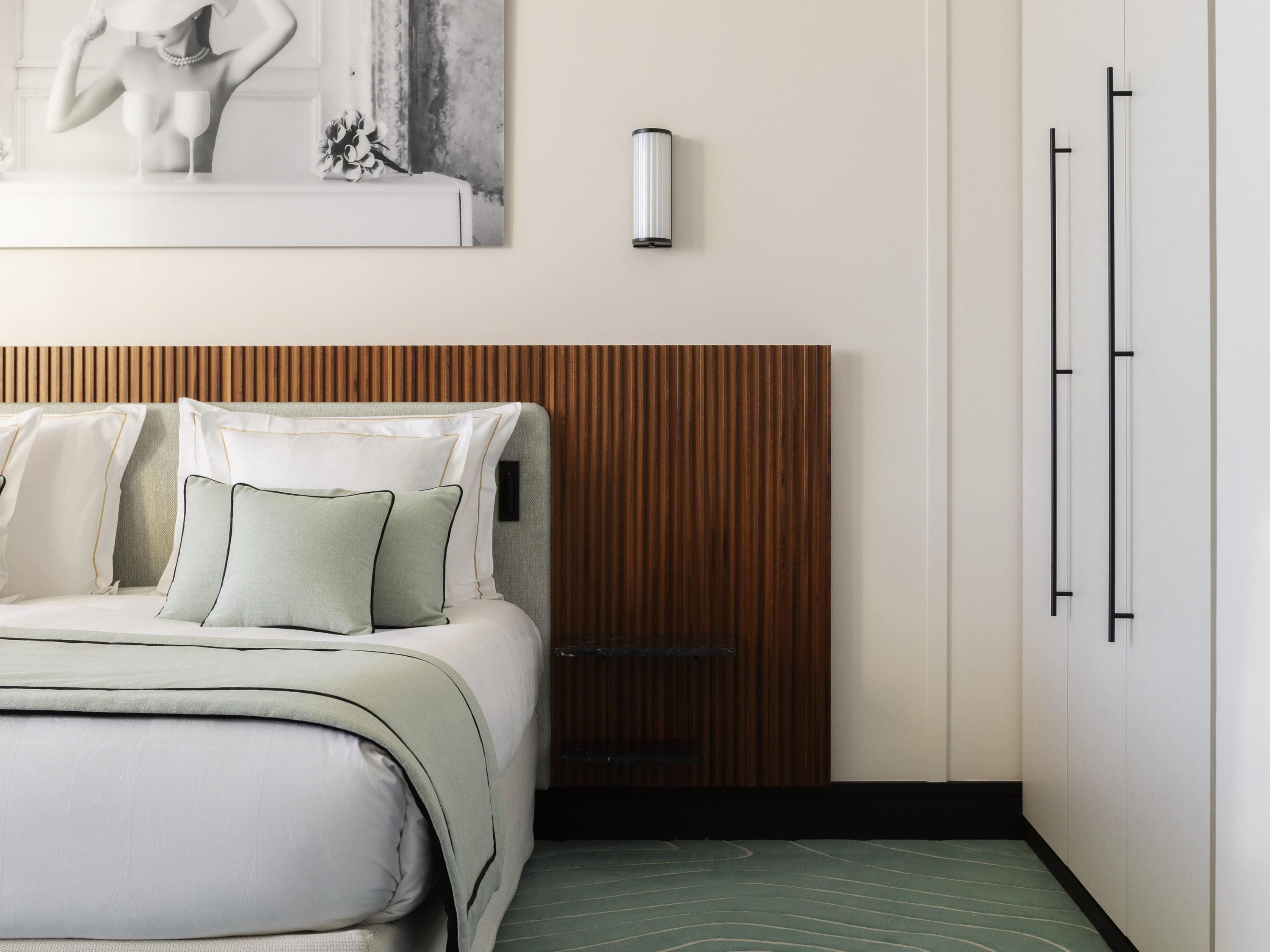 Une chambre à coucher avec un lit, des oreillers, une tête de lit en bois, une lampe fixée au mur et une porte.