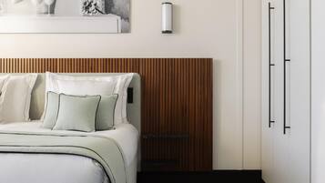Une chambre à coucher avec un lit, des oreillers, une tête de lit en bois, une lampe fixée au mur et une porte.