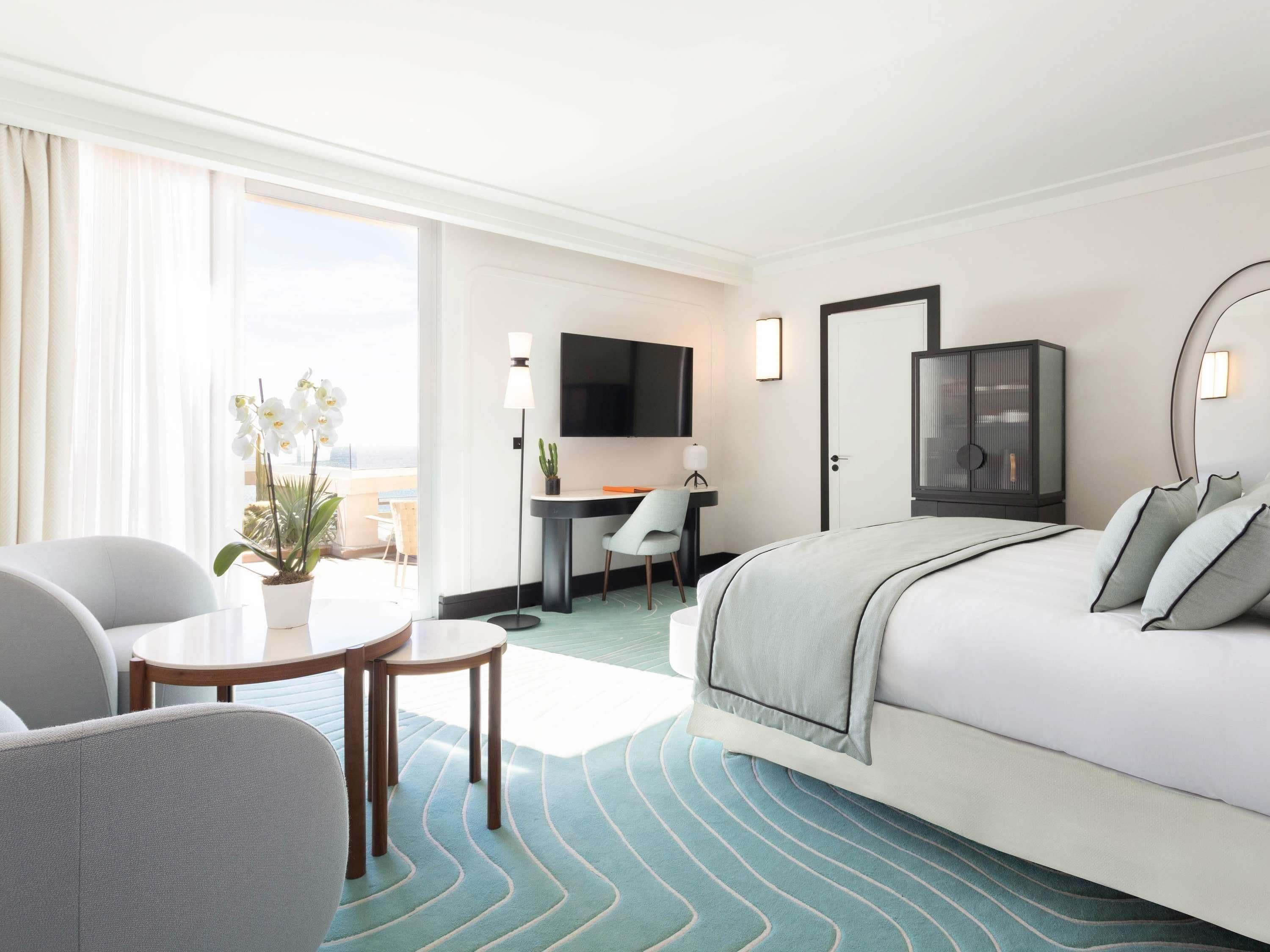 A hotel room with a bed, desk, chair, TV, and a view of the outdoors.