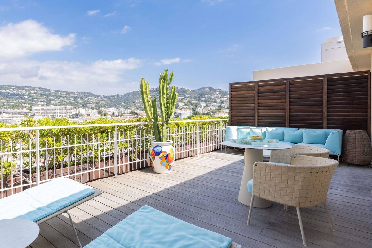 A rooftop terrace with a view of a cityscape, a cactus plant, and outdoor furniture.