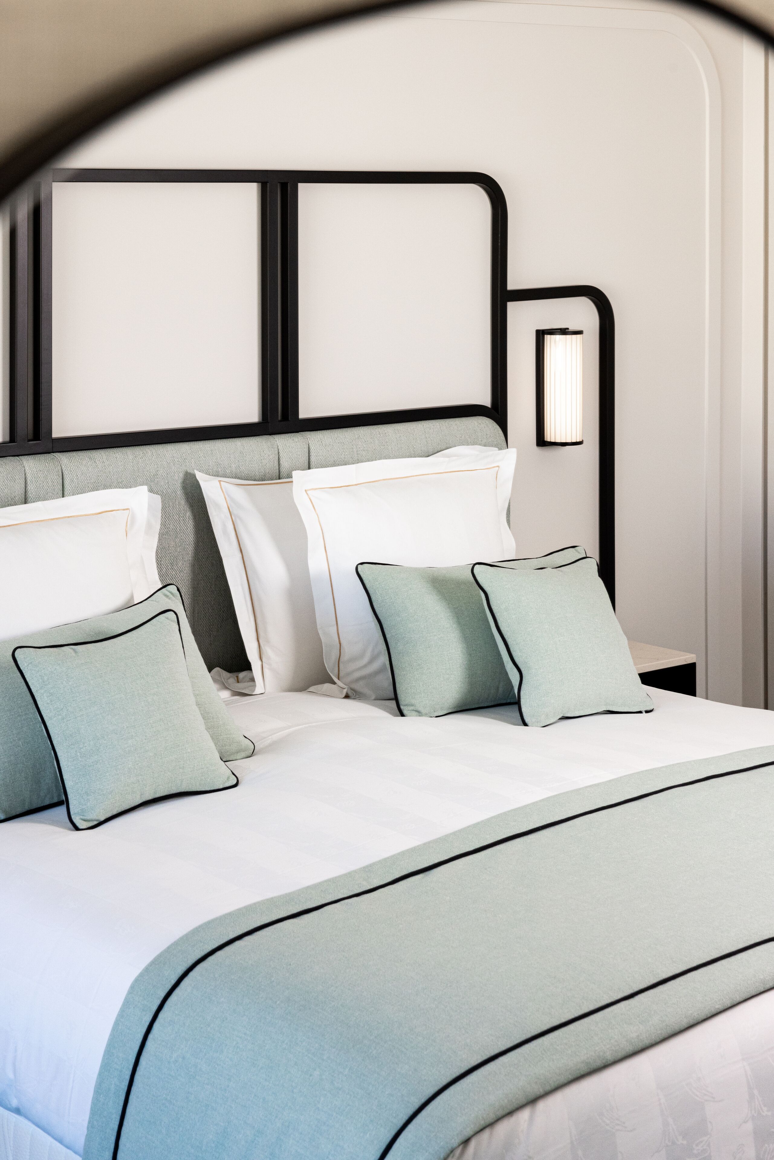 A neatly made bed with a headboard, pillows, and a bedside lamp.