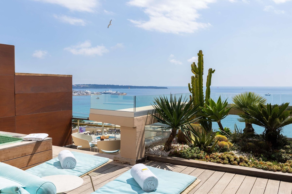A rooftop terrace with a pool, sun loungers, and a view of the sea.
