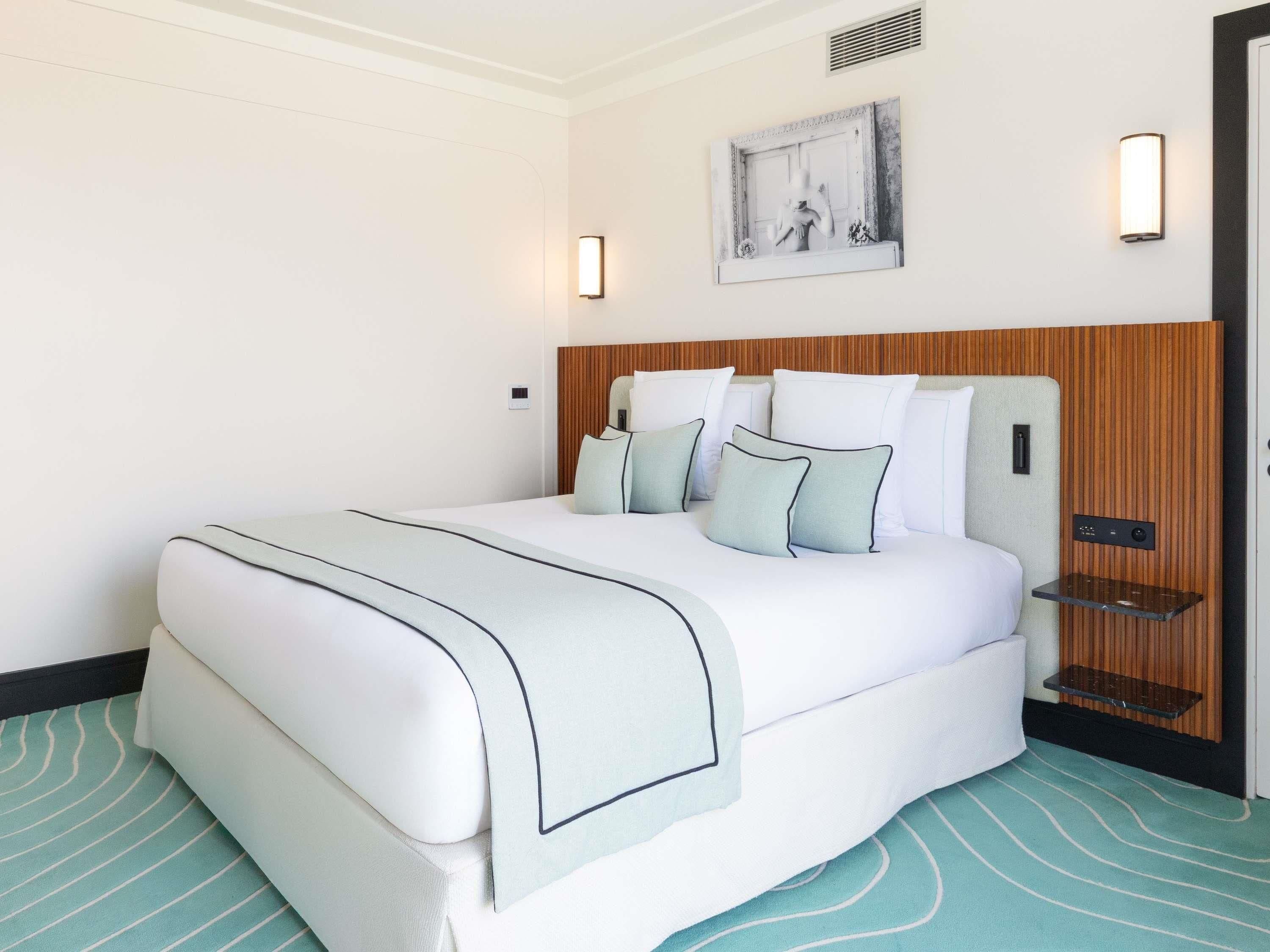 Una habitación de hotel con una cama, cabecera, una obra de arte en la pared y una mesita de noche.