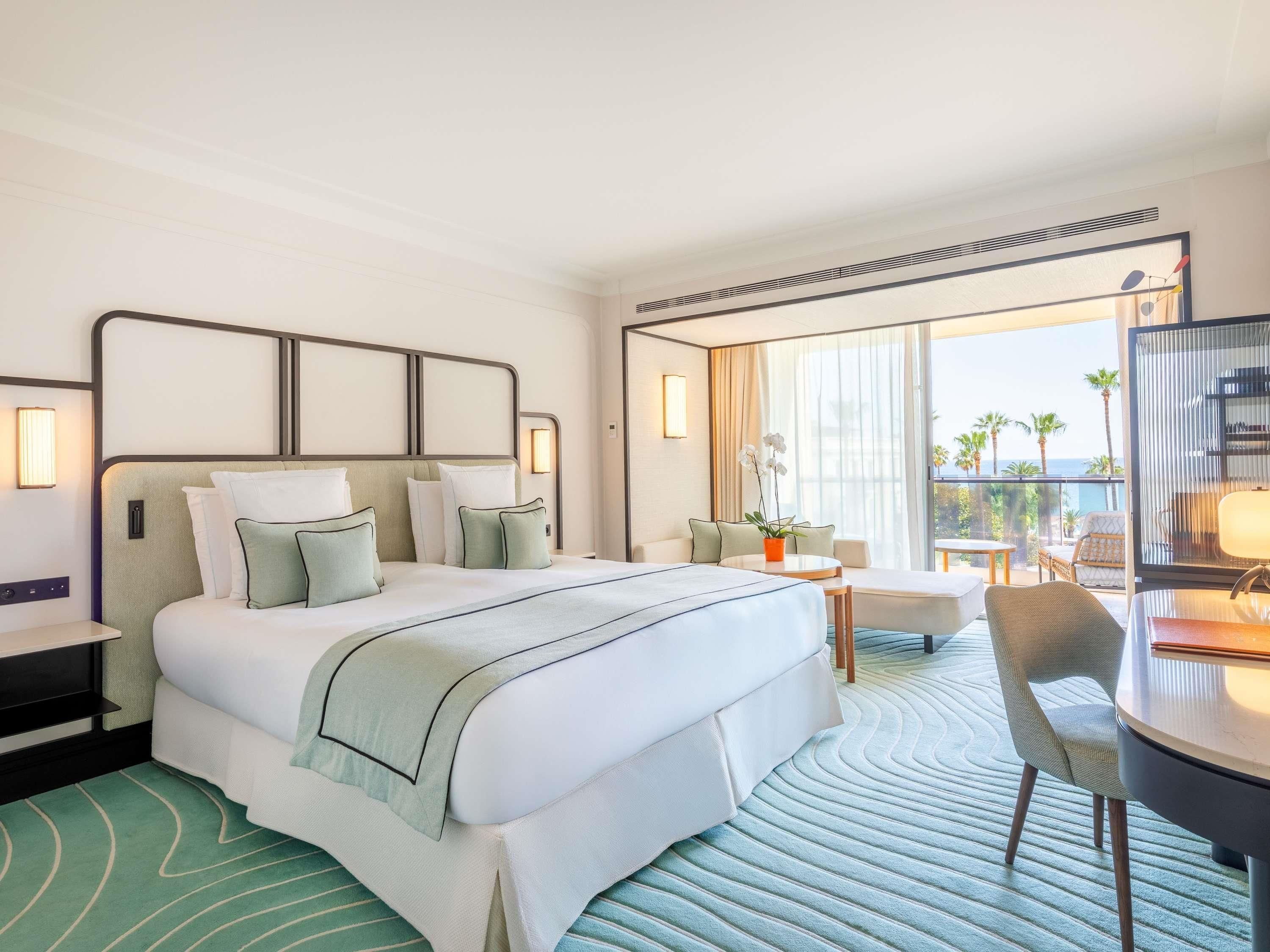 Een hotelkamer met een groot bed, een bureau, een stoel, een kleine tafel en een balkon met uitzicht.