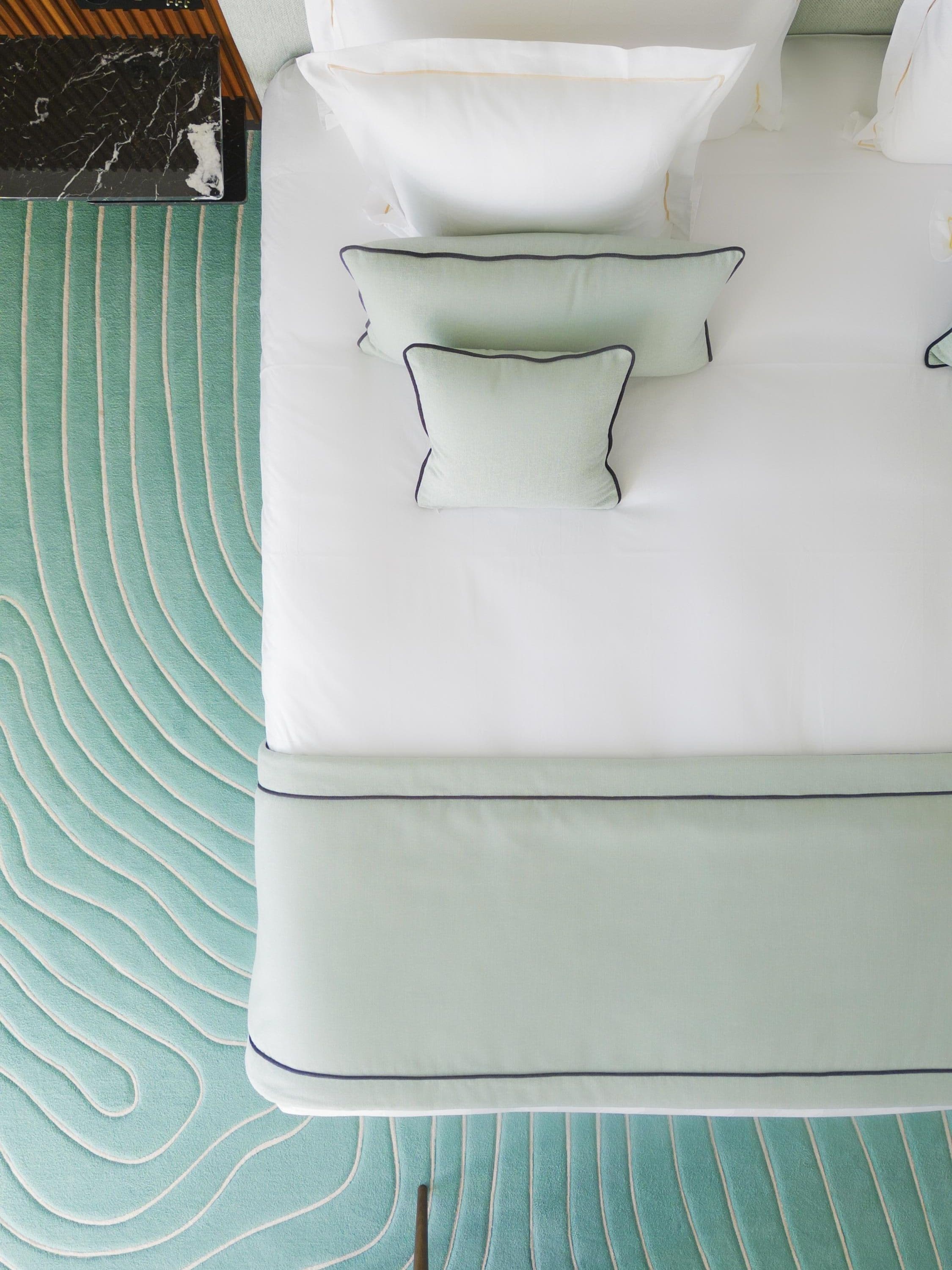 A bed with a green patterned bedspread and white pillows with dark trim.