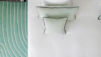 A bed with a green patterned bedspread and white pillows with dark trim.