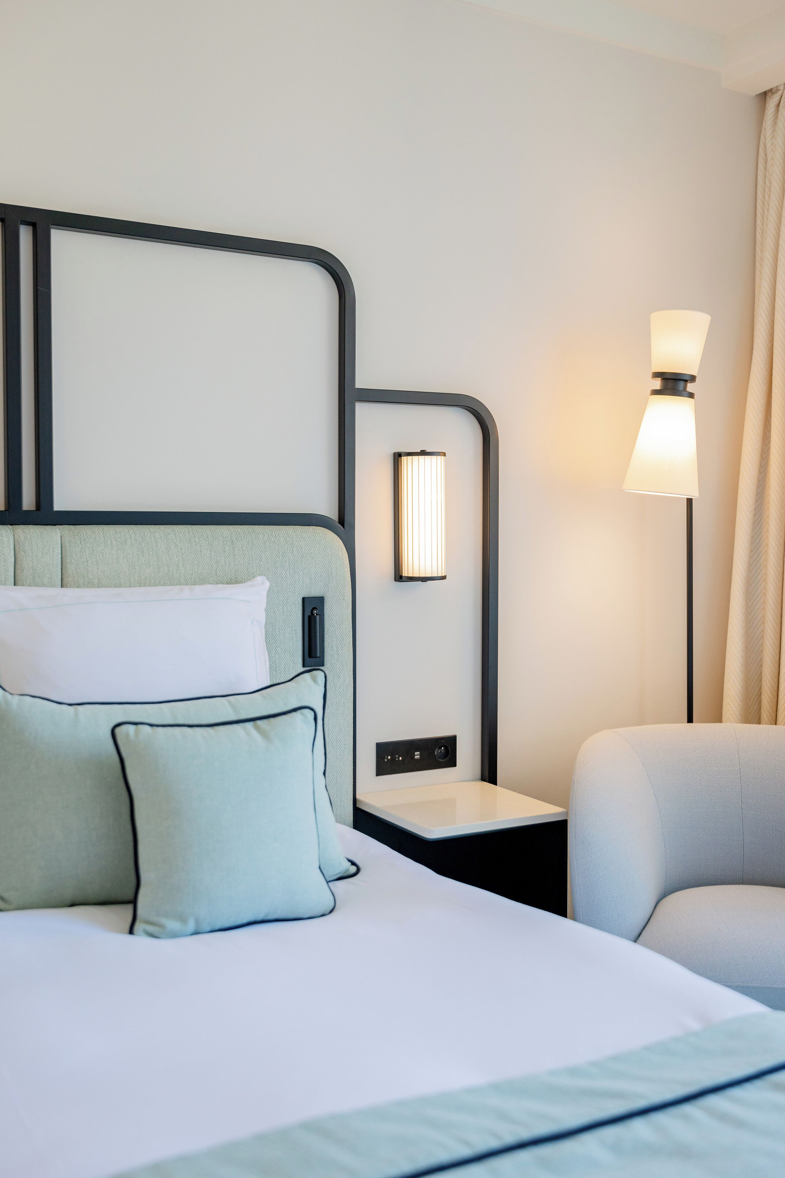 A hotel room with a bed, a nightstand, a lamp, and a chair.