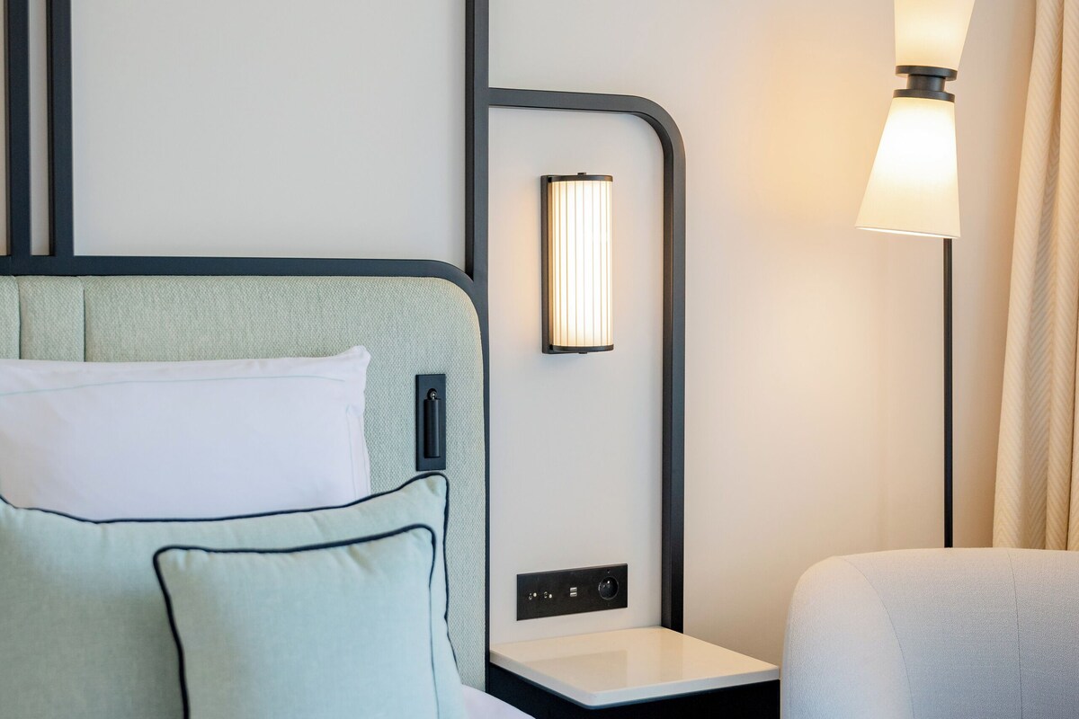 A hotel room with a bed, a nightstand, a lamp, and a chair.