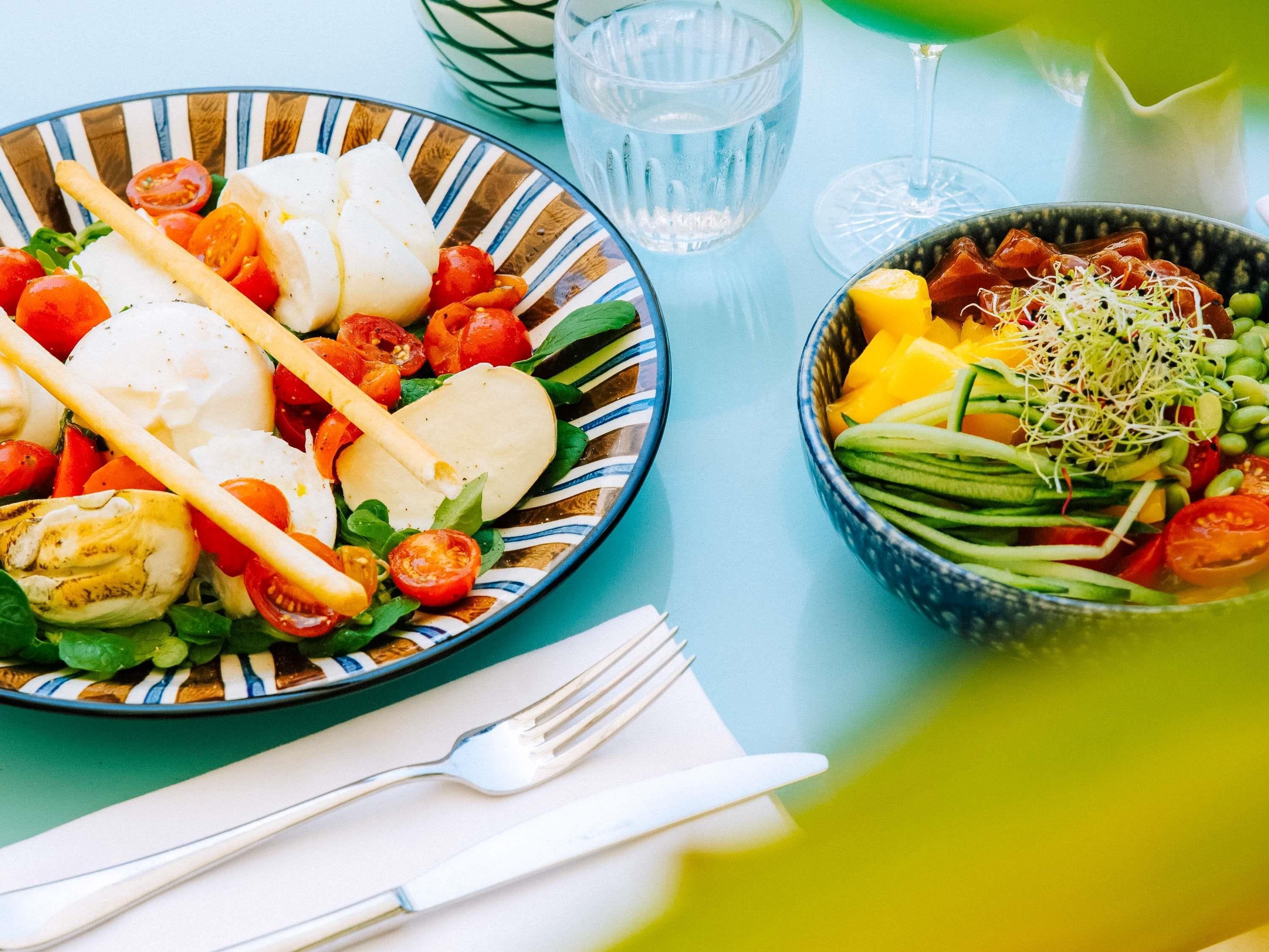 A table with a plate of food, a bowl of salad, and a glass of water.