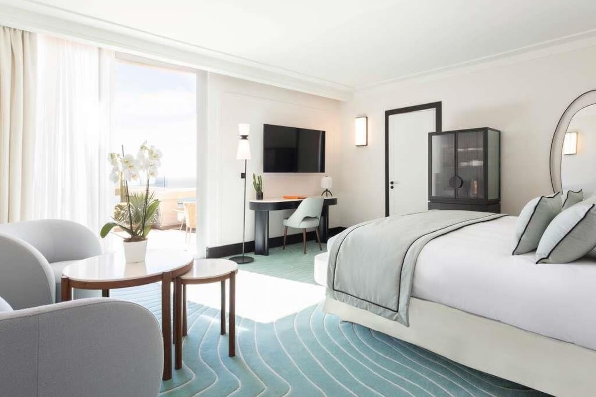 A hotel room with a bed, a desk, a chair, a TV, and a window.