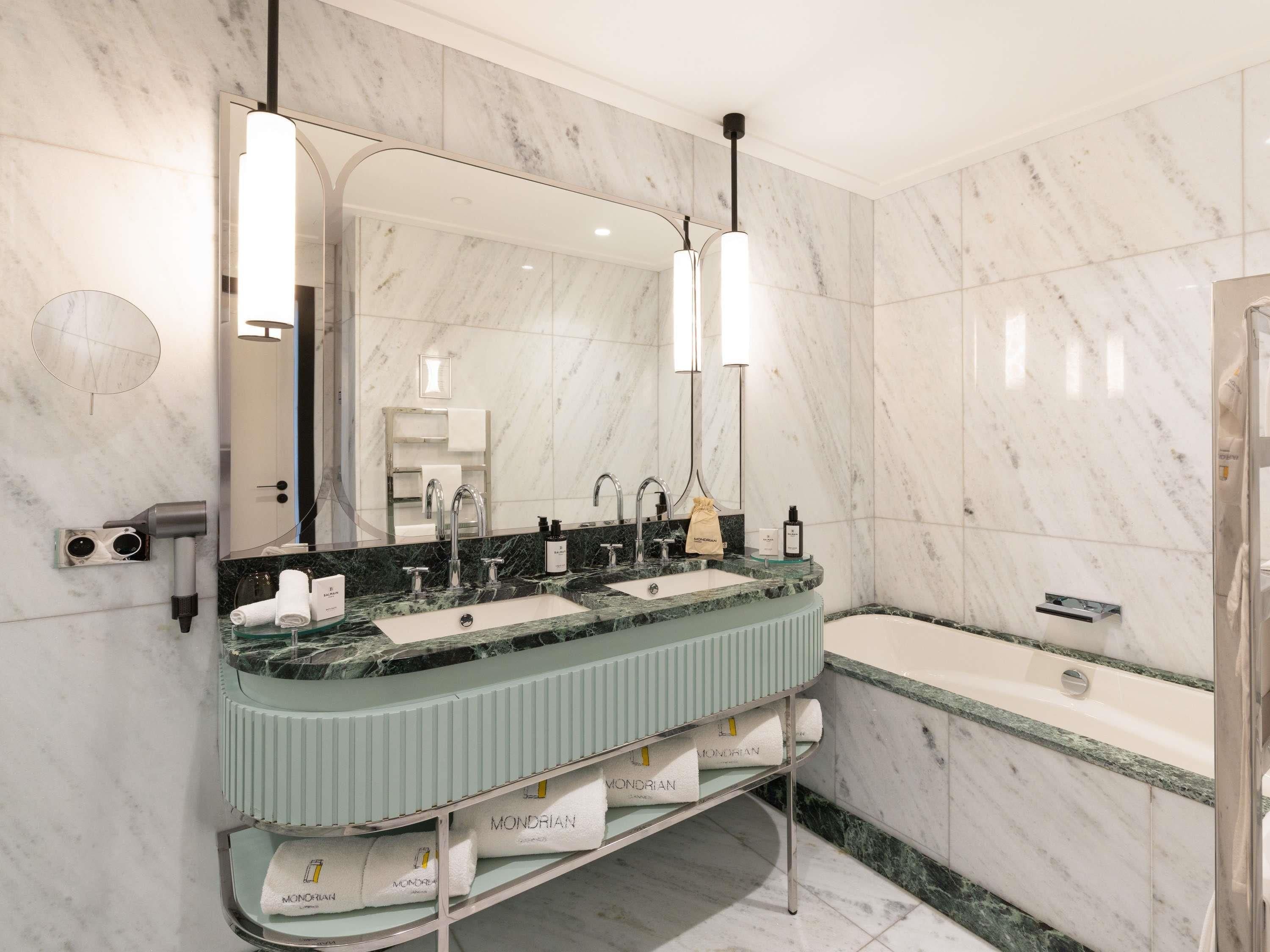 Ein modernes Badezimmer mit Marmorwand, einem großen Spiegel, einem Waschbecken mit Platz für zwei Personen, einem Handtuchhalter und einer Badewanne.