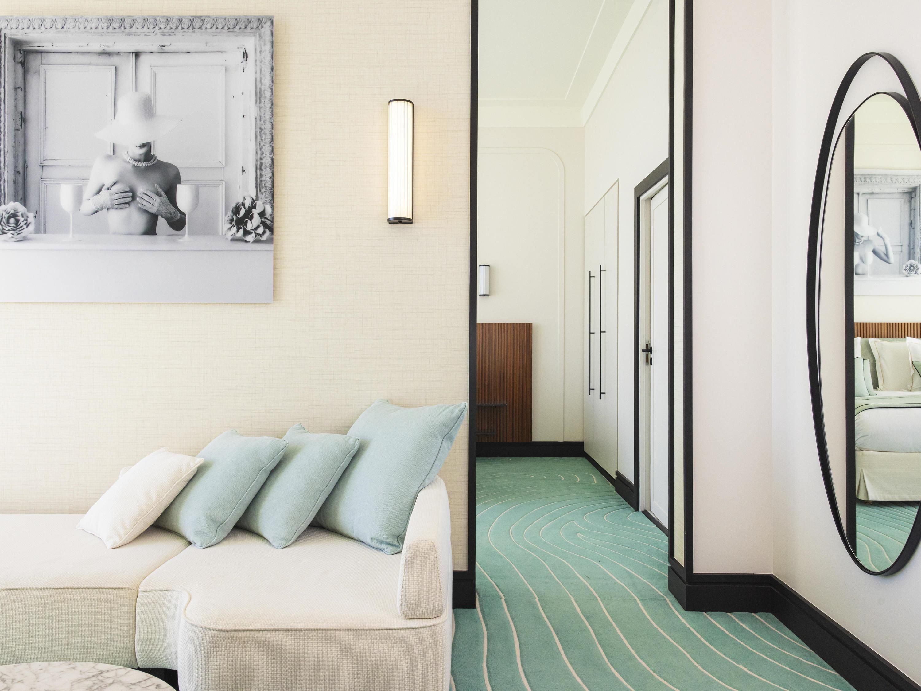 A hotel room with a white sofa, a mirror, and a green-striped carpet.