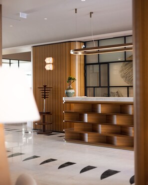A modern lobby with a wooden reception desk, a potted plant, and a minimalist staircase.