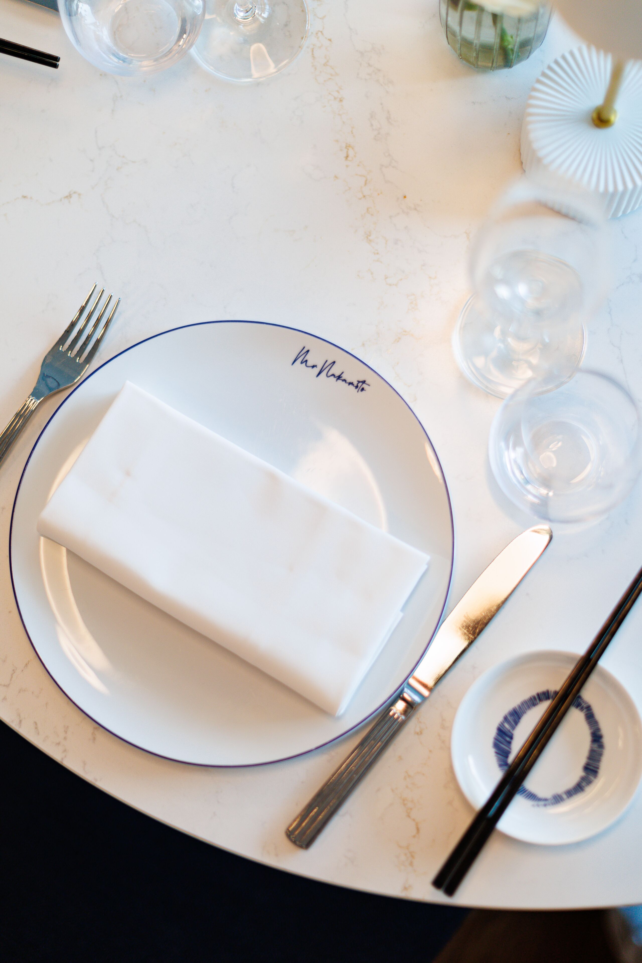 A table set with a folded napkin, a fork, a knife, and a spoon on a plate with a blue rim.