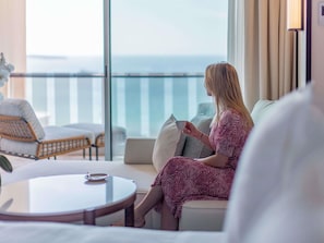 Una mujer sentada en una silla de balcón, sosteniendo una taza, con vista al mar.
