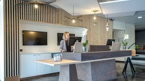A reception desk with a flat-screen TV, a computer, and a vase with white flowers. - Mercure Cavaillon Hotel (Cavaillon)