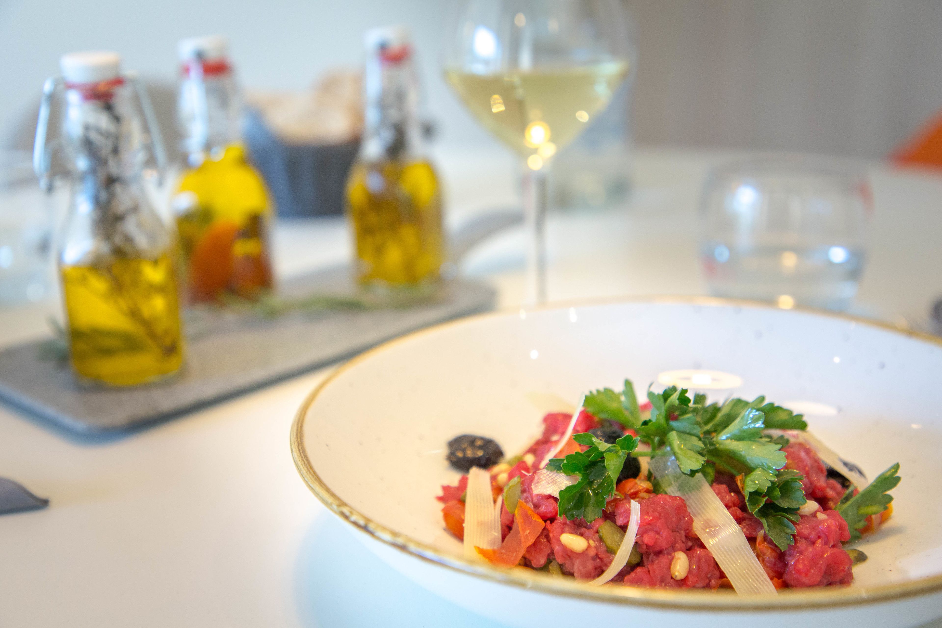 A dining table with a plate of food, three bottles of olive oil, and a glass of white wine.