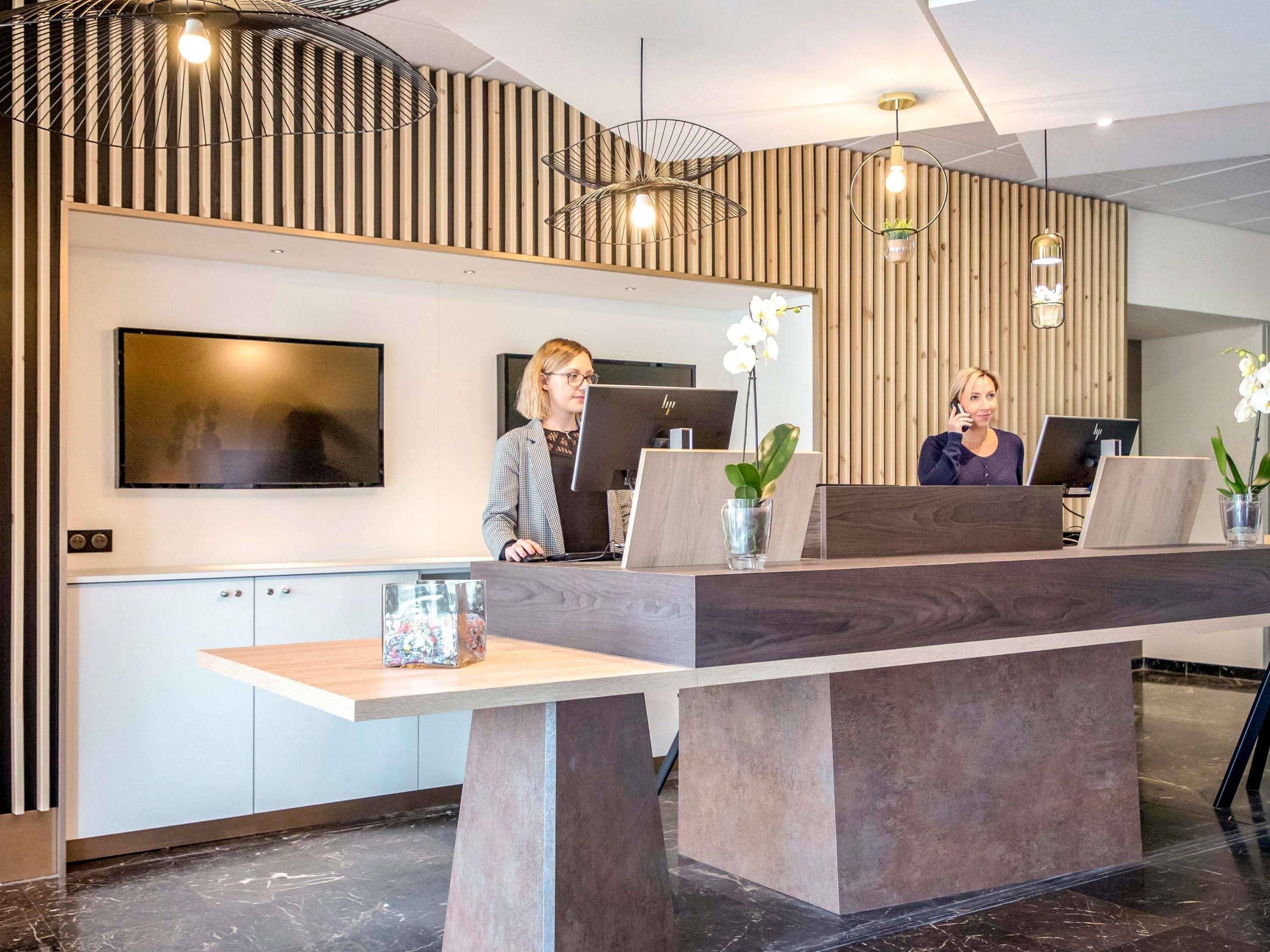 A reception desk with two computer stations, a TV mounted on the wall, and a modern ceiling design.