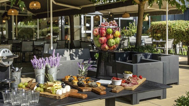 Een buitenterras met diverse gerechten en dranken, waaronder een fruitschaal, kaas en vleesschotels.