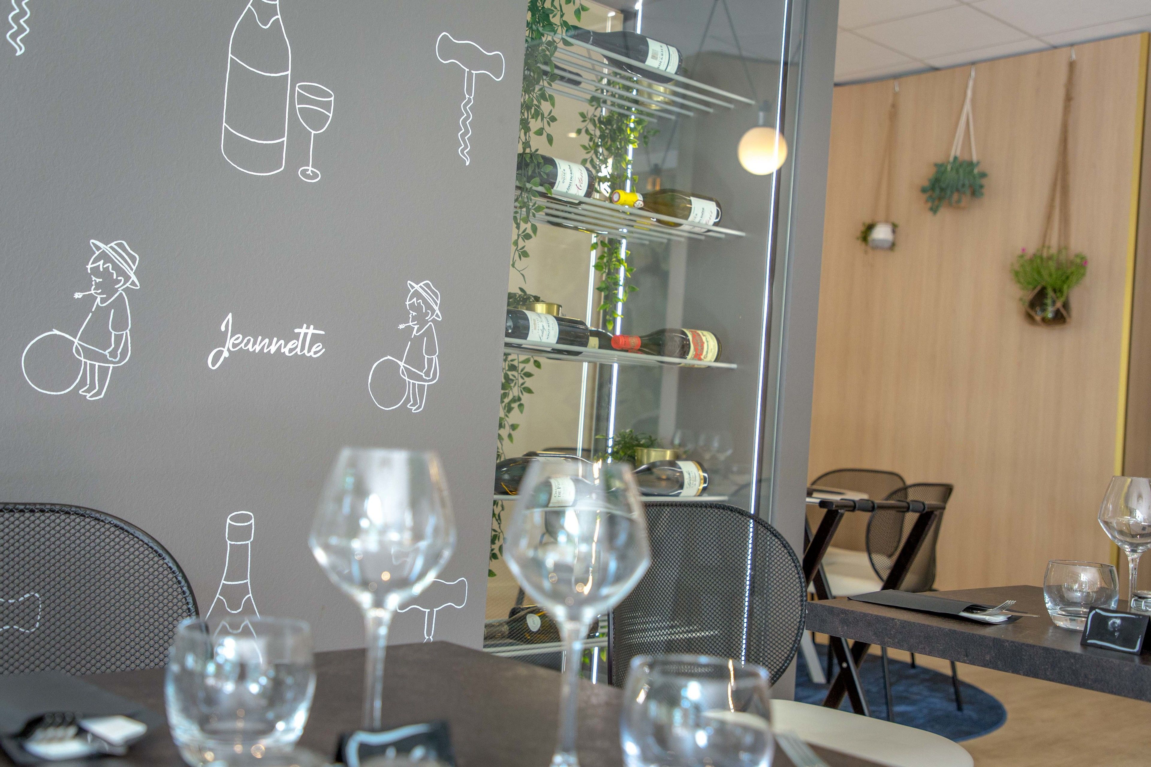 Ein Restaurantinneres mit einem für zwei Personen gedeckten Tisch, Weingläsern, einer Weinflasche und einem Menüständer.