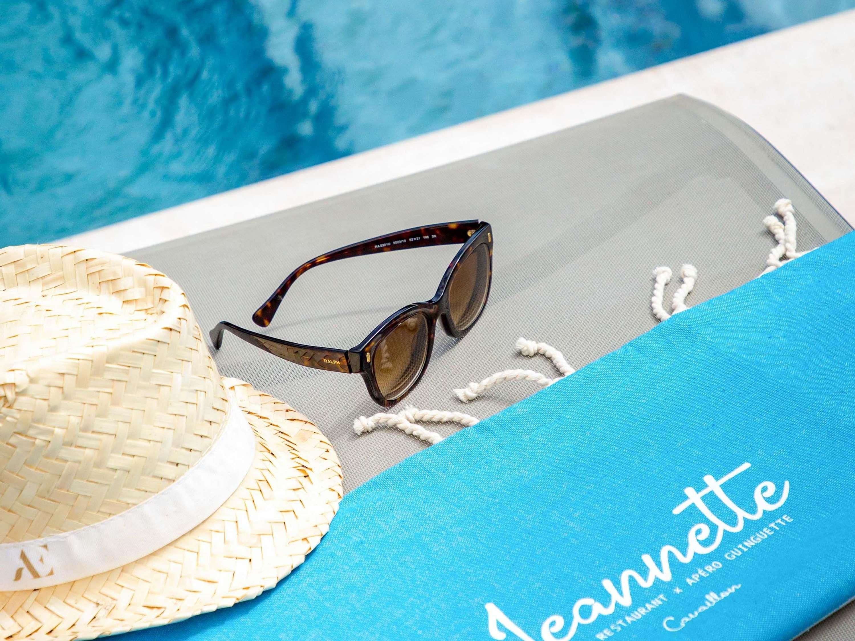 Un sombrero de paja trenzada, gafas de sol y una toalla azul con la palabra 'Jeannette' escrita.
