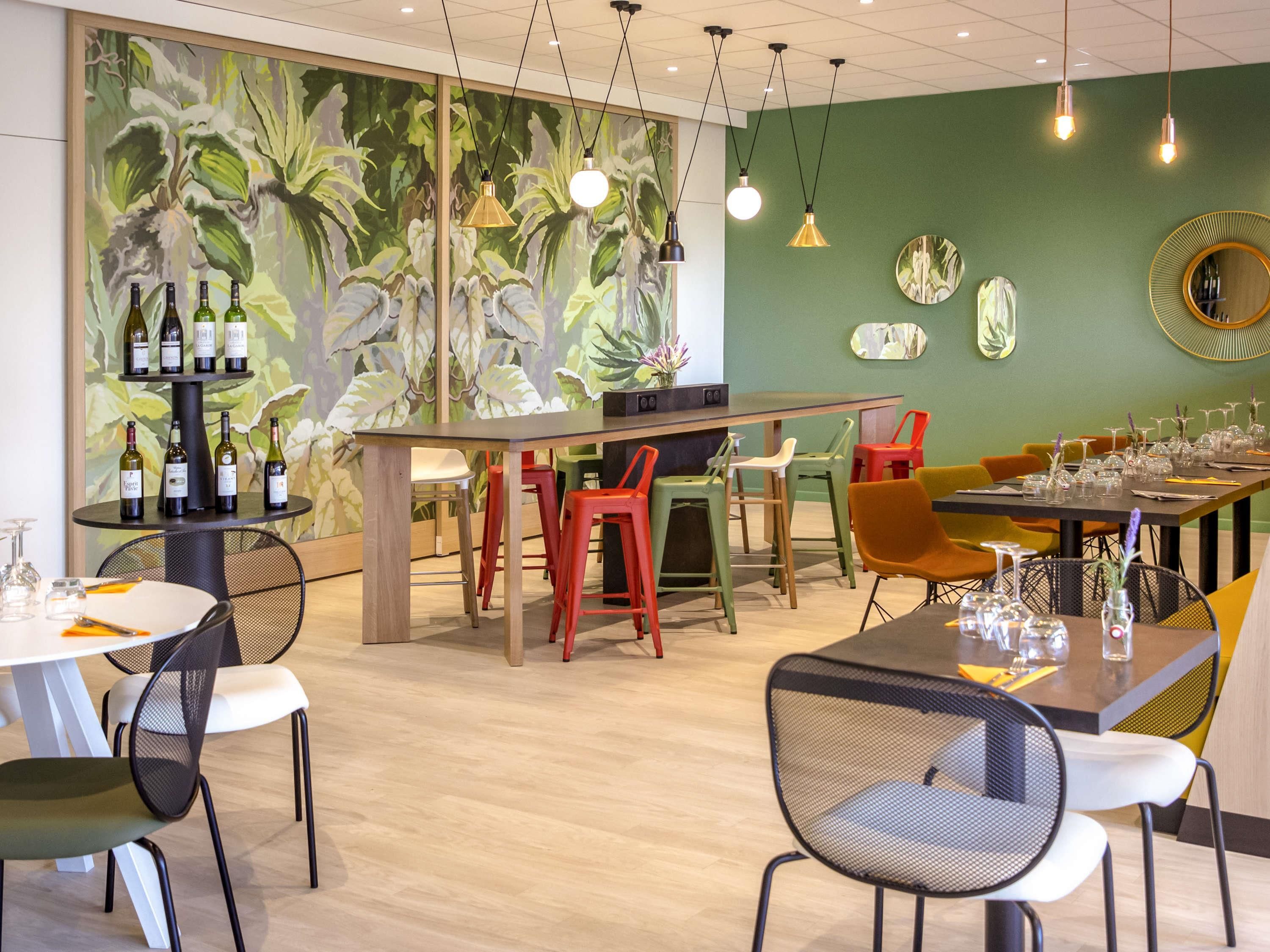 Een restaurant met een groene muurschildering, meerdere eettafels en stoelen.