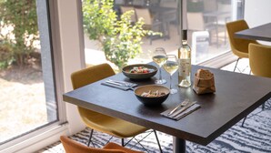 Een eettafel met een saladeschaal, een fles wijn en een broodje.