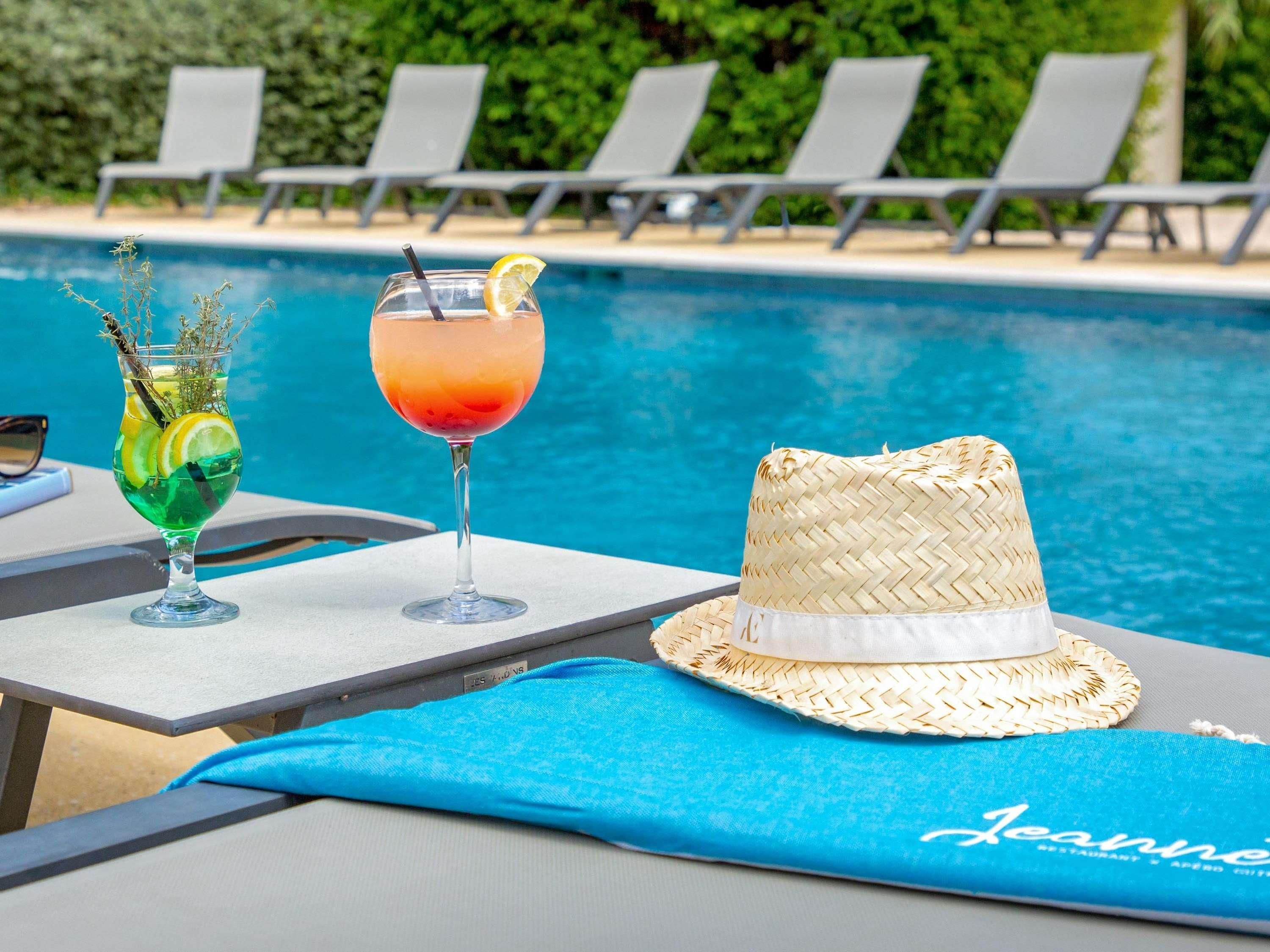 Escena junto a la piscina con dos bebidas, un sombrero de paja y sillas reclinables.