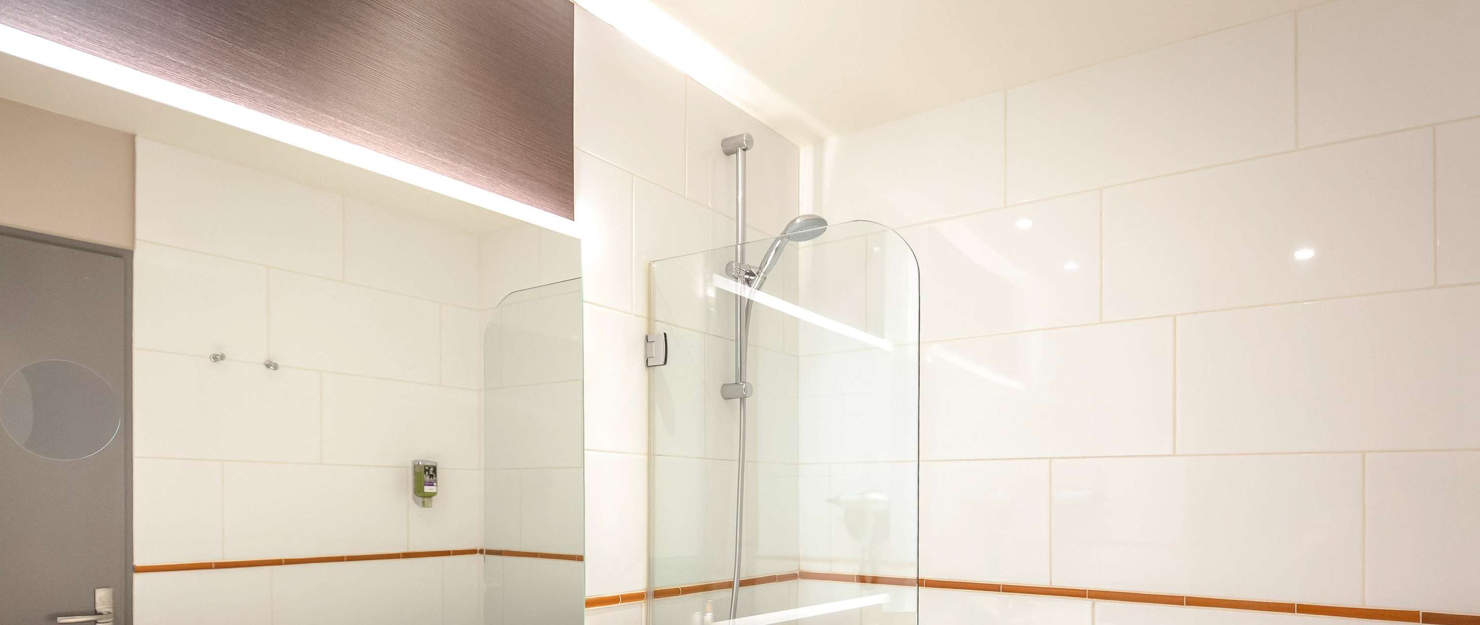 Une salle de bain moderne avec des carreaux blancs, une douche en verre et un bord en bois le long des plinthes.