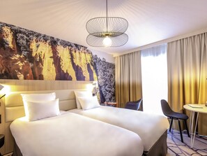 A hotel room with a large bed, a desk, and a chair. There is a painting on the wall and a window with curtains. - Mercure Cavaillon Hotel (Cavaillon)