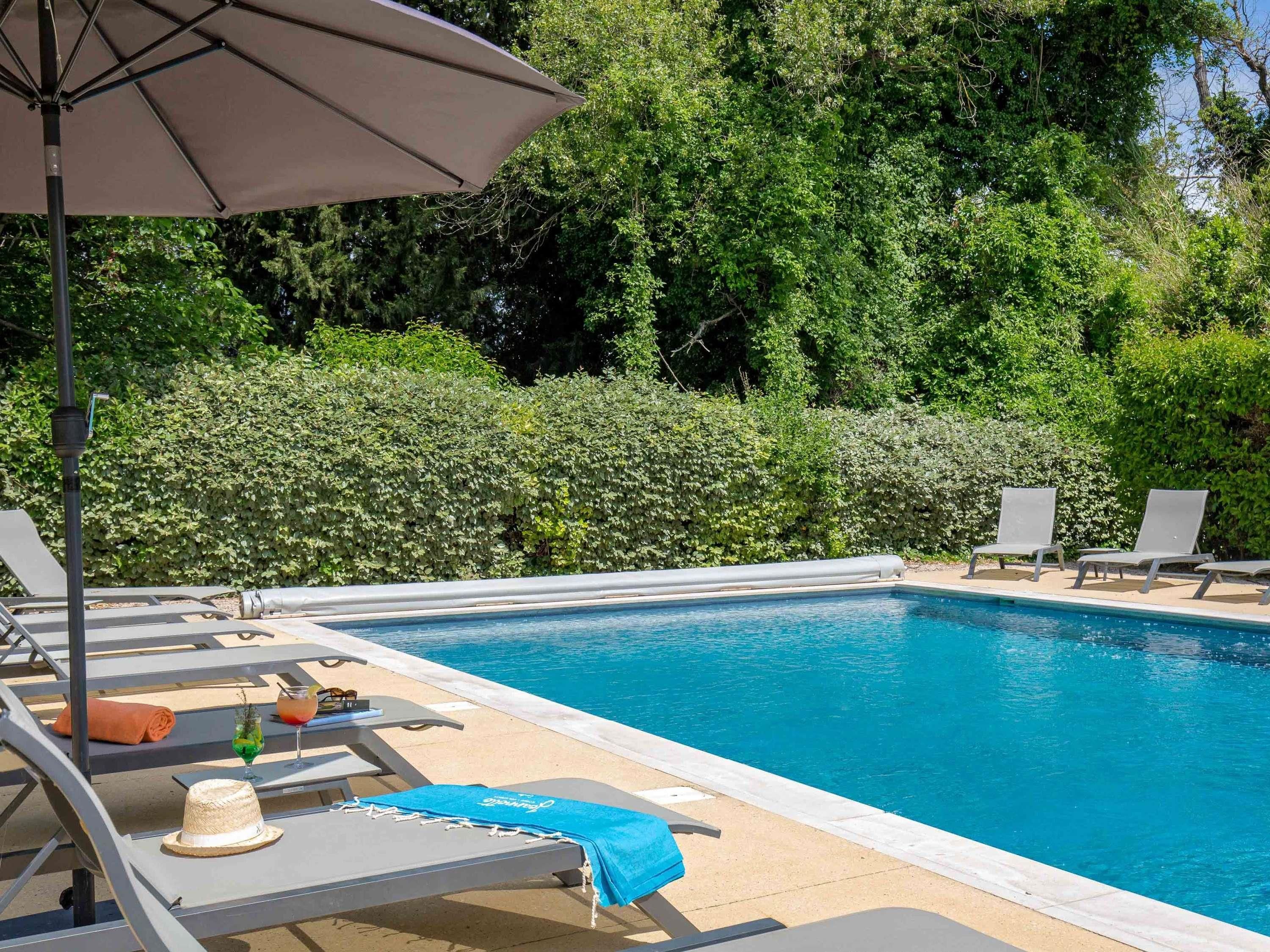 A swimming pool with lounge chairs and a table, surrounded by greenery.