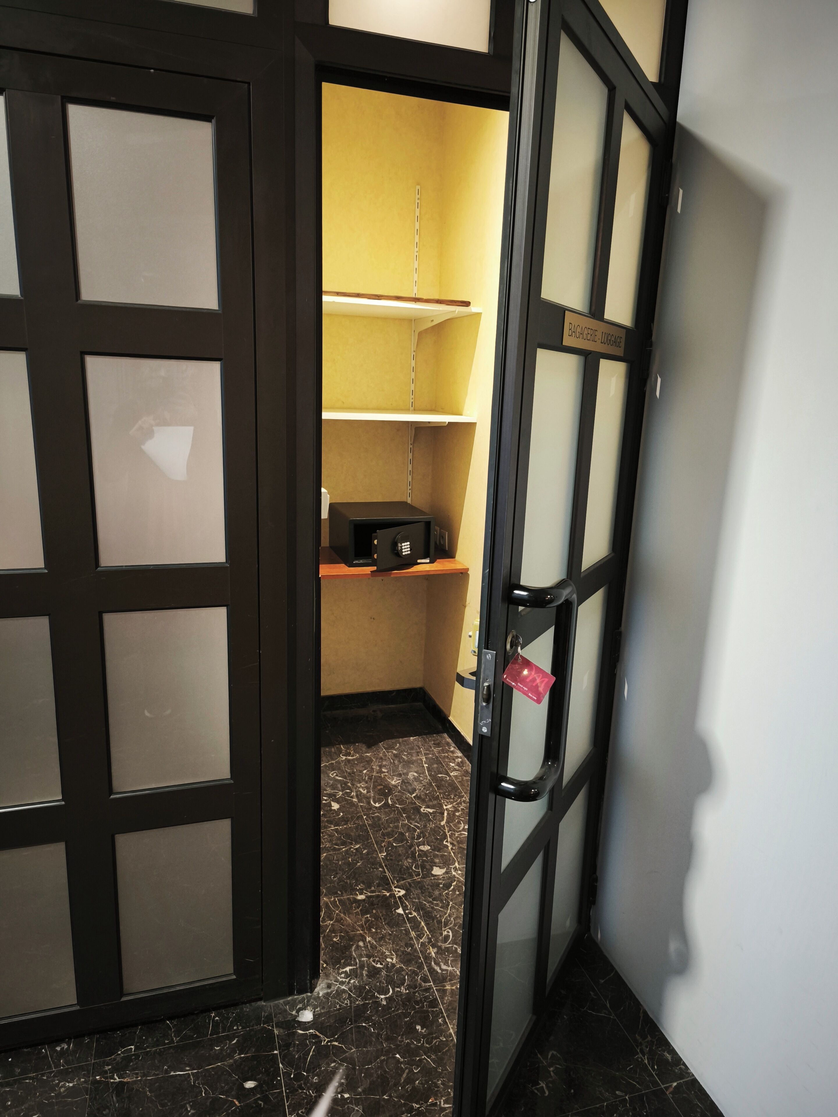 A hotel room with a marble floor, a black-framed door, and a luggage storage area with shelves.